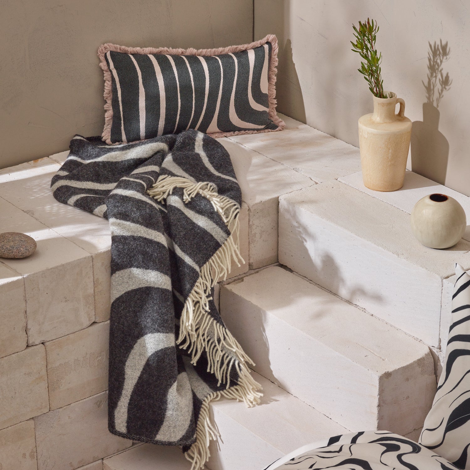 Nanson villainen beige-musta Syli -torkkupeitto ja -koristetyynynpäällinen, kauniissa asetelmassa.