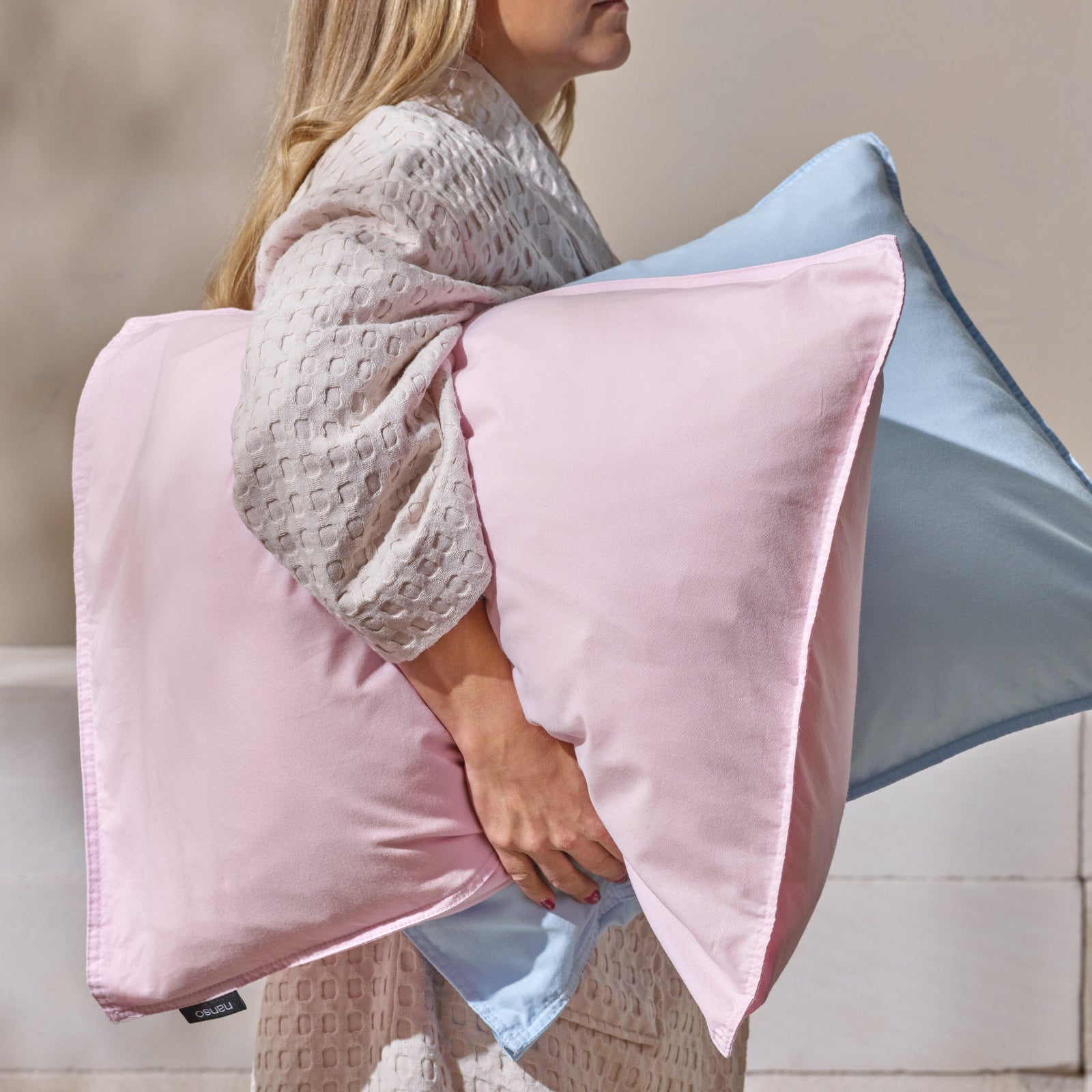 Nanson pastellisävyiset Uni -tyynyliinat sekä vohveli-kylpytakki esillä mallin yllä. Tyynyt naisen kainalossa, kuvattuna sivusta päin.