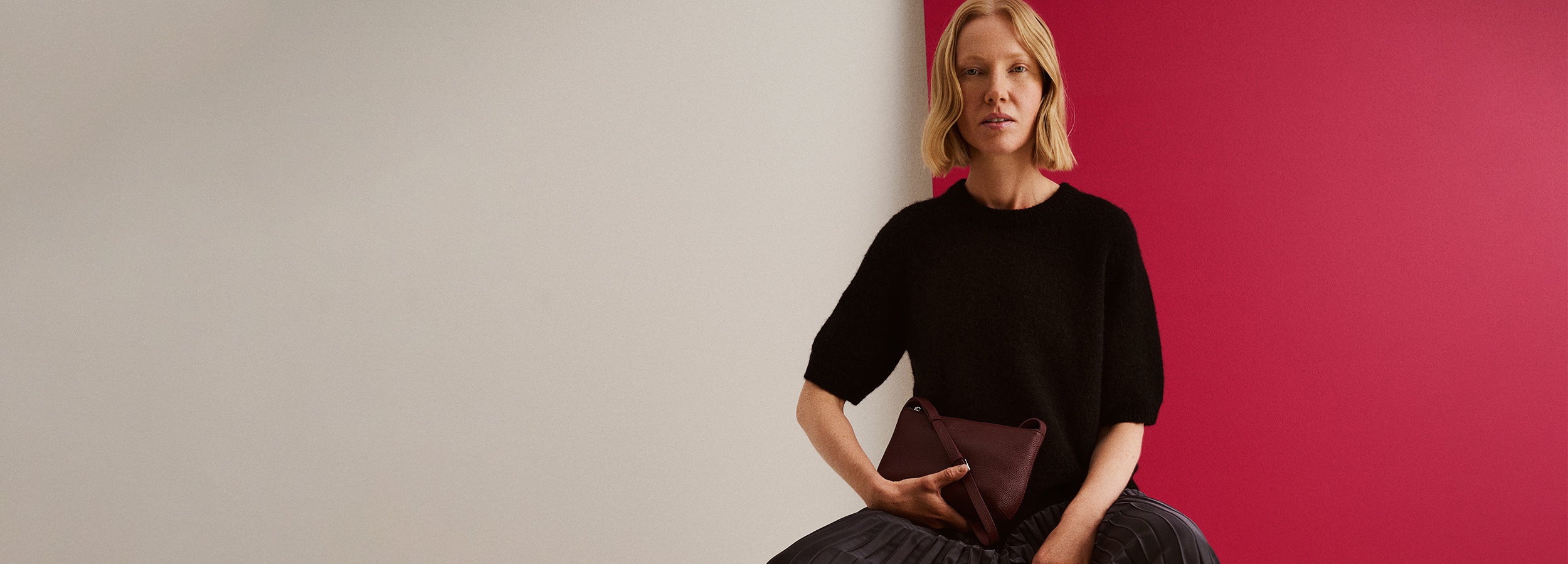 Nanson lyhythihainen musta Tuohi-neulepusero mallin päällä, kädessä viininpunainen Naru olkalaukku.