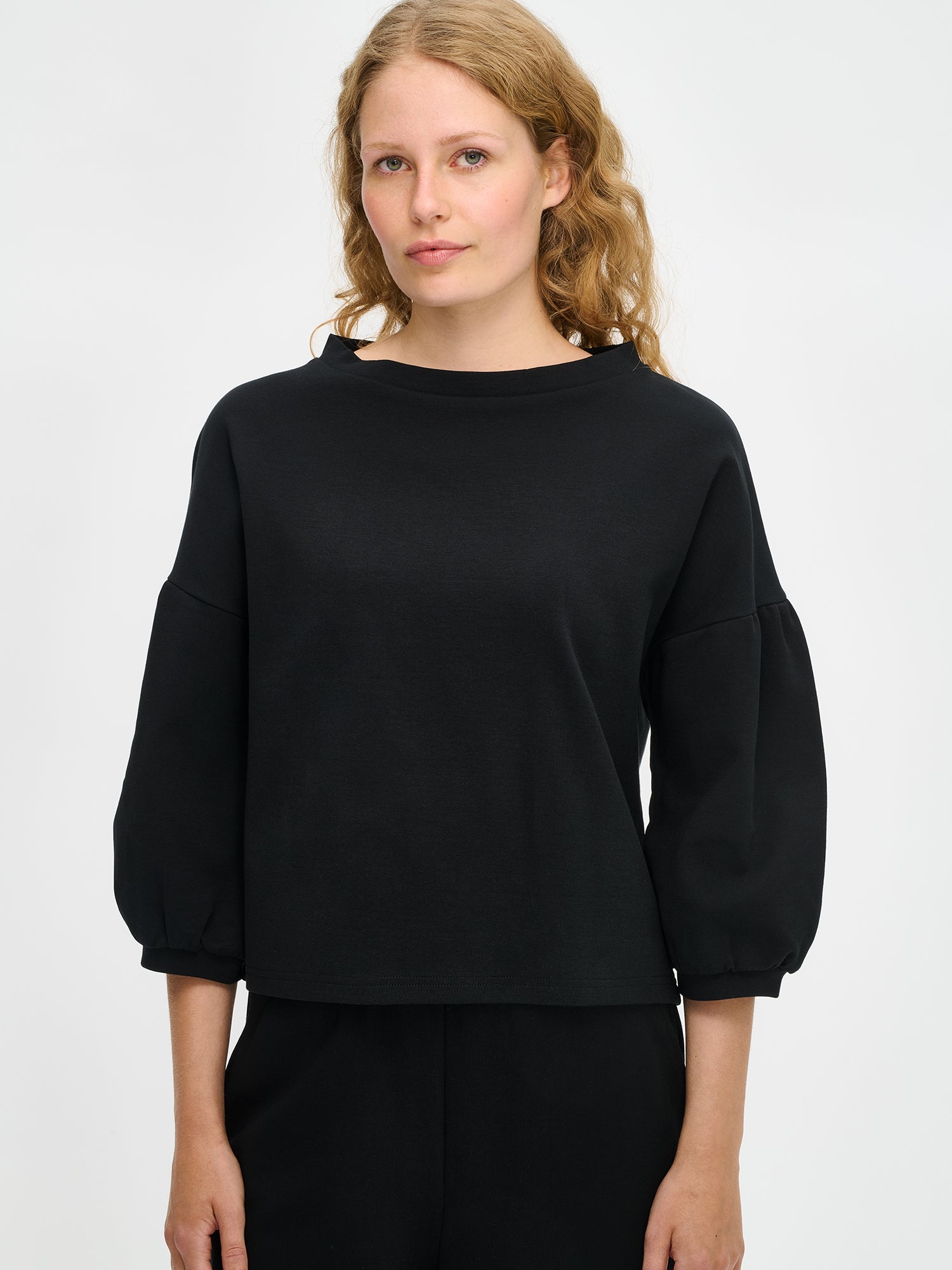 Nanson naisten musta Leija-pusero mallin yllä lähikuvassa, venepääntie ja poimutetut 3/4-hihat paksummassa interlock-neuloksessa.