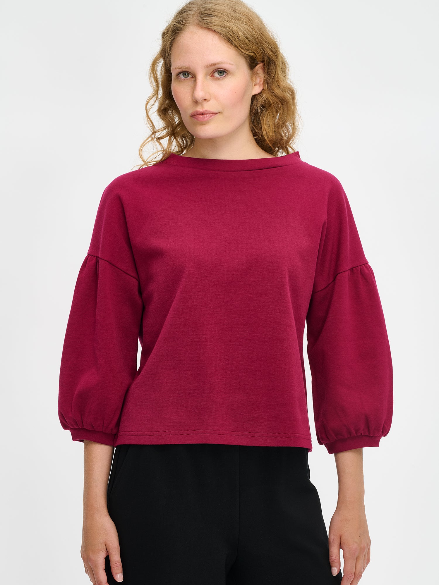 Nanson naisten viininpunainen Leija-pusero mallin yllä lähikuvassa, venemuotoinen pystykaulus ja poimutetut 3/4 pituiset hihat näkyvissä interlock-neuloksessa.