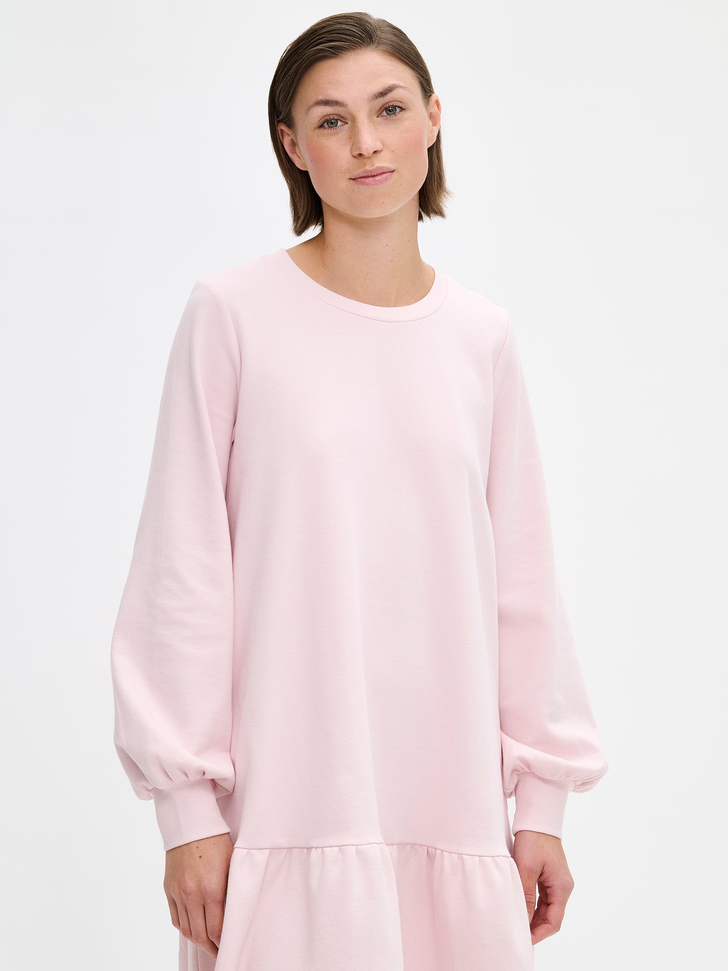 Nanson naisten rento Leija-mekko. Lyhyessä mekossa on pyöreä pääntie, sivuissa taskut, helmassa poimutus ja kauniisti hihansuihin poimuttuvat täyspitkät hihat. Kuvattuna läheltä mallin päällä edestä päin.