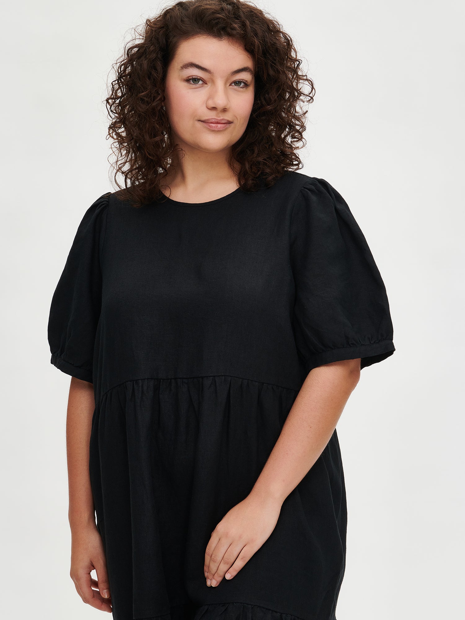 Nanson naisten kaunis musta Sarastus-pellavamekko volyymisilla frillakerroksilla ja lyhyillä puhvihihoilla mallin päällä koossa XL lähikuvassa.
