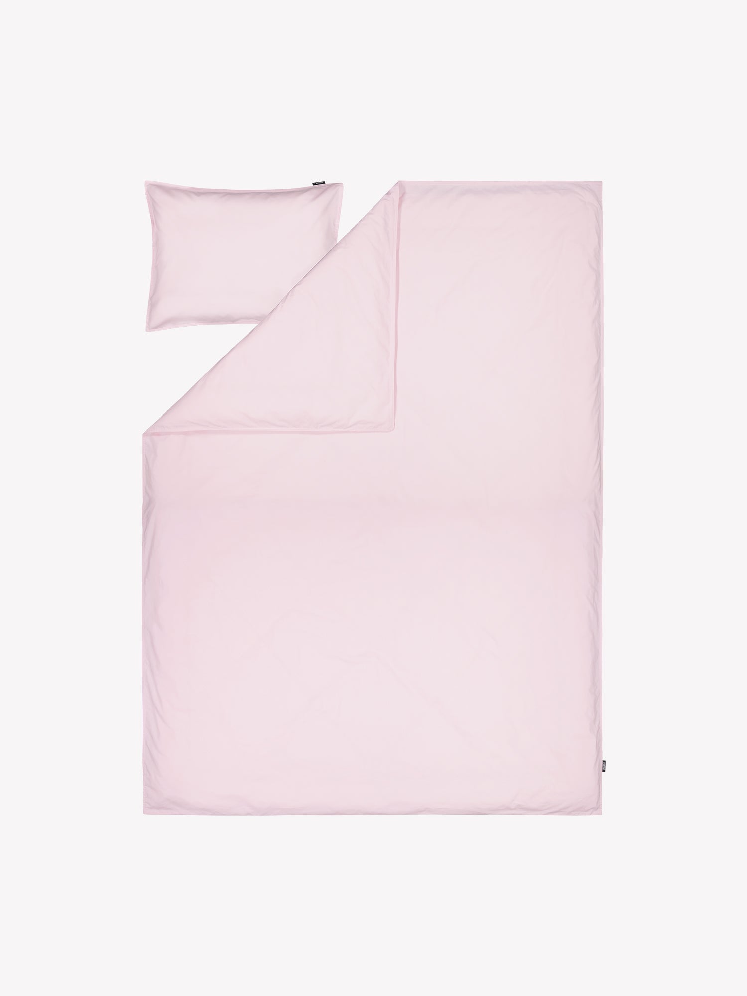 Nanson vaaleanpunainen Uni-pussilakana kivipestystä tiiviistä ja korkealaatuisesta puuvillakankaasta tuotekuvassa täkin ja tyynyn päällä.