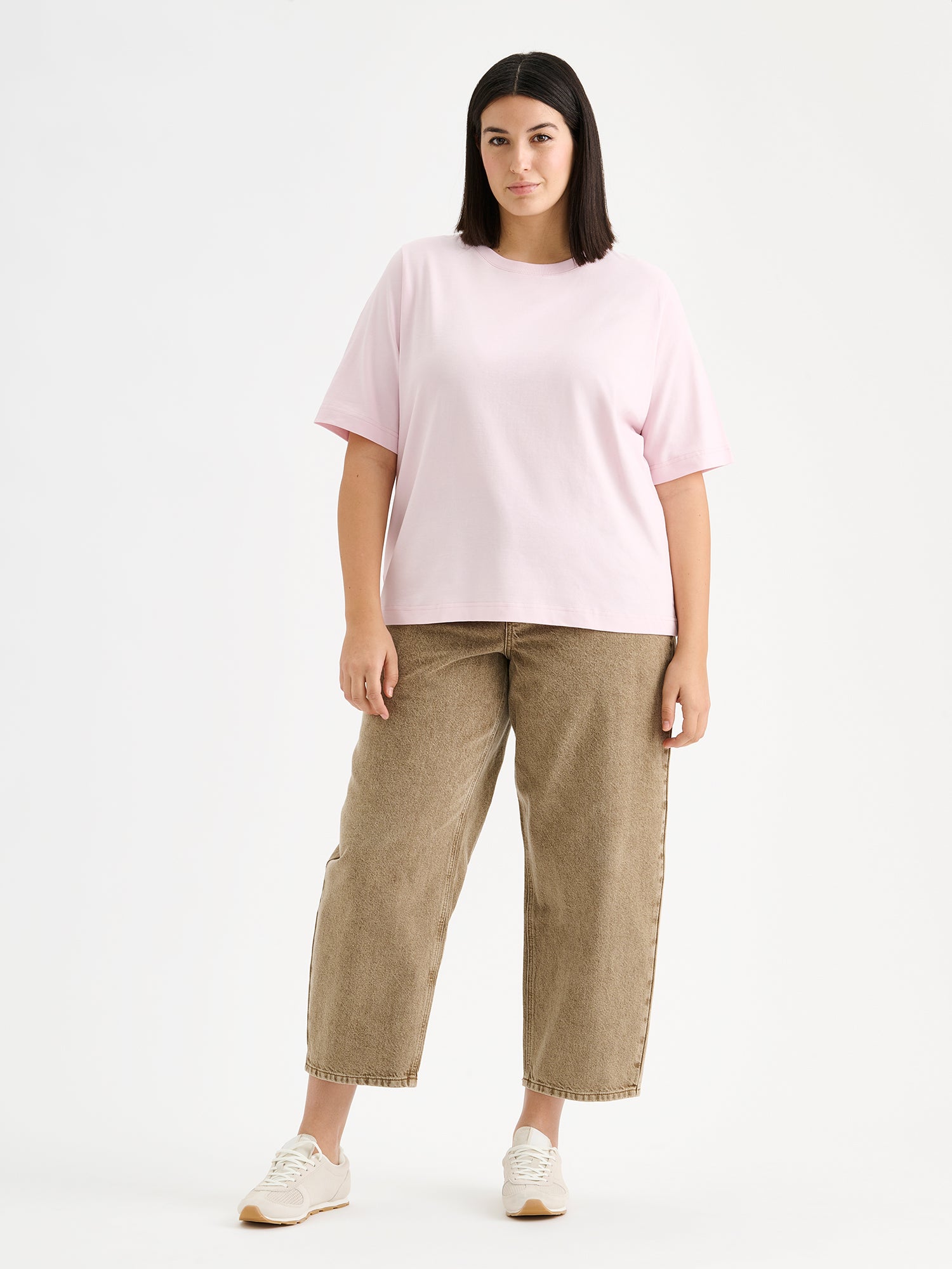 nanson vaaleanpunainen Normi T-paita mallin päällä ruskeiden farkkujen kanssa.