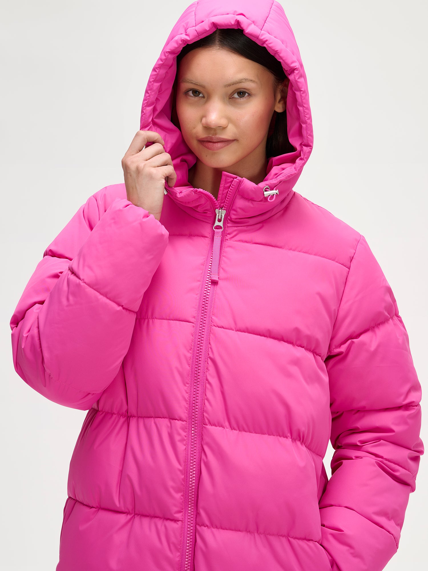 Lämmin ja muhkea pitkä pinkki Lumi-toppatakki miellyttävän kevyellä vanuvuorella. Mallin päällä edestä ja huppu päällä.