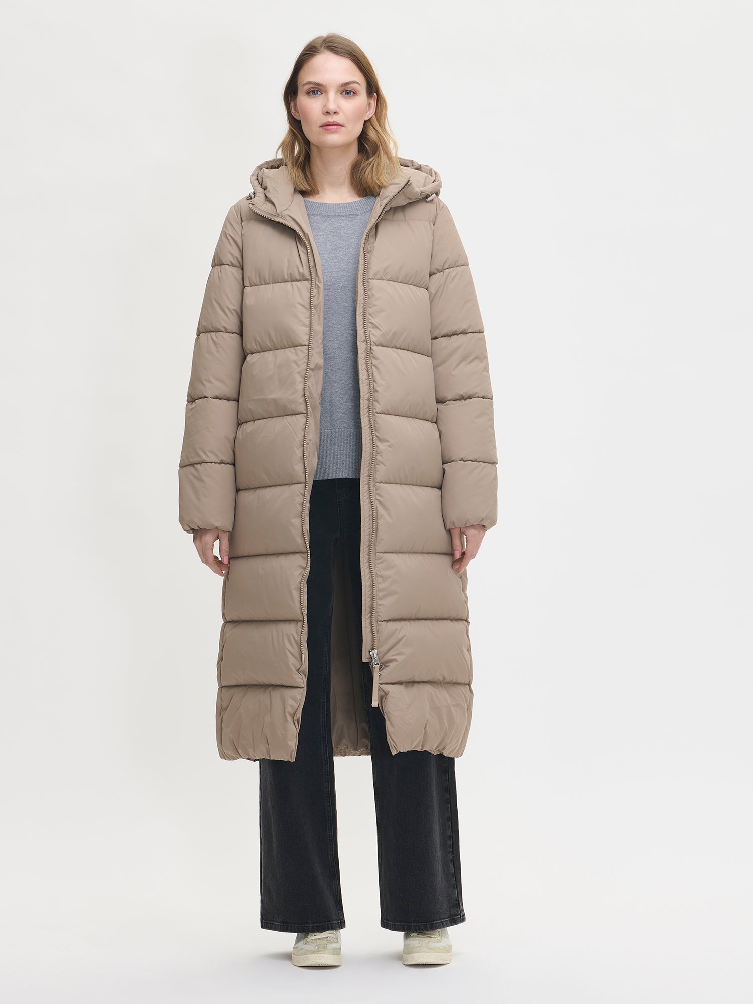 Lämmin ja muhkea pitkä beige Lumi-toppatakki miellyttävän kevyellä vanuvuorella. Mallin päällä edestä ja takki auki.