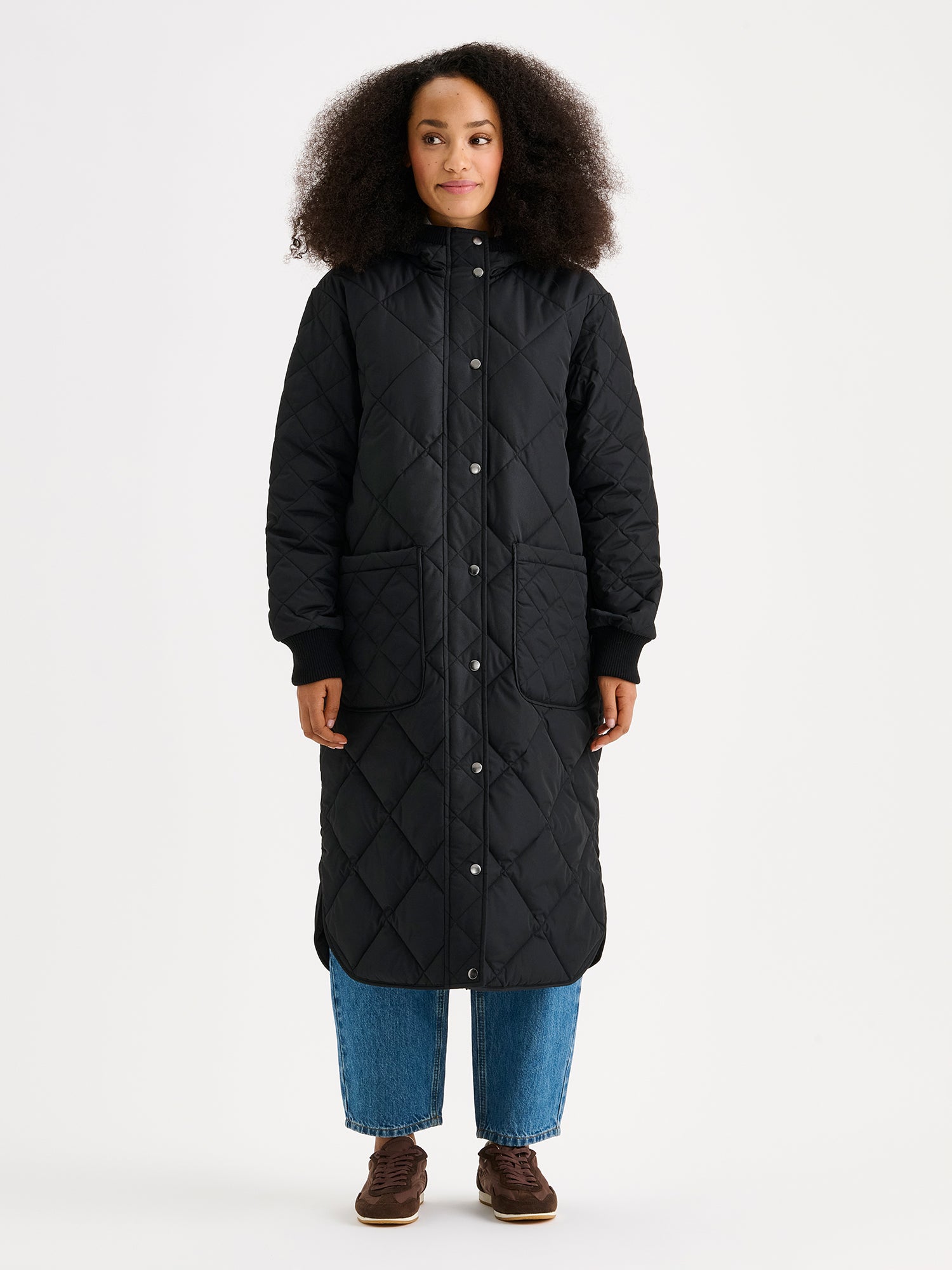 Nanson naisten rennon tyylikäs musta Maxi Hood-tikkitakki kevyellä vanulla ja lämpimällä hupulla. Hupullinen tikkitakki on täydellinen valinta välikauteen. Mallin päällä edestä kuvattuna.