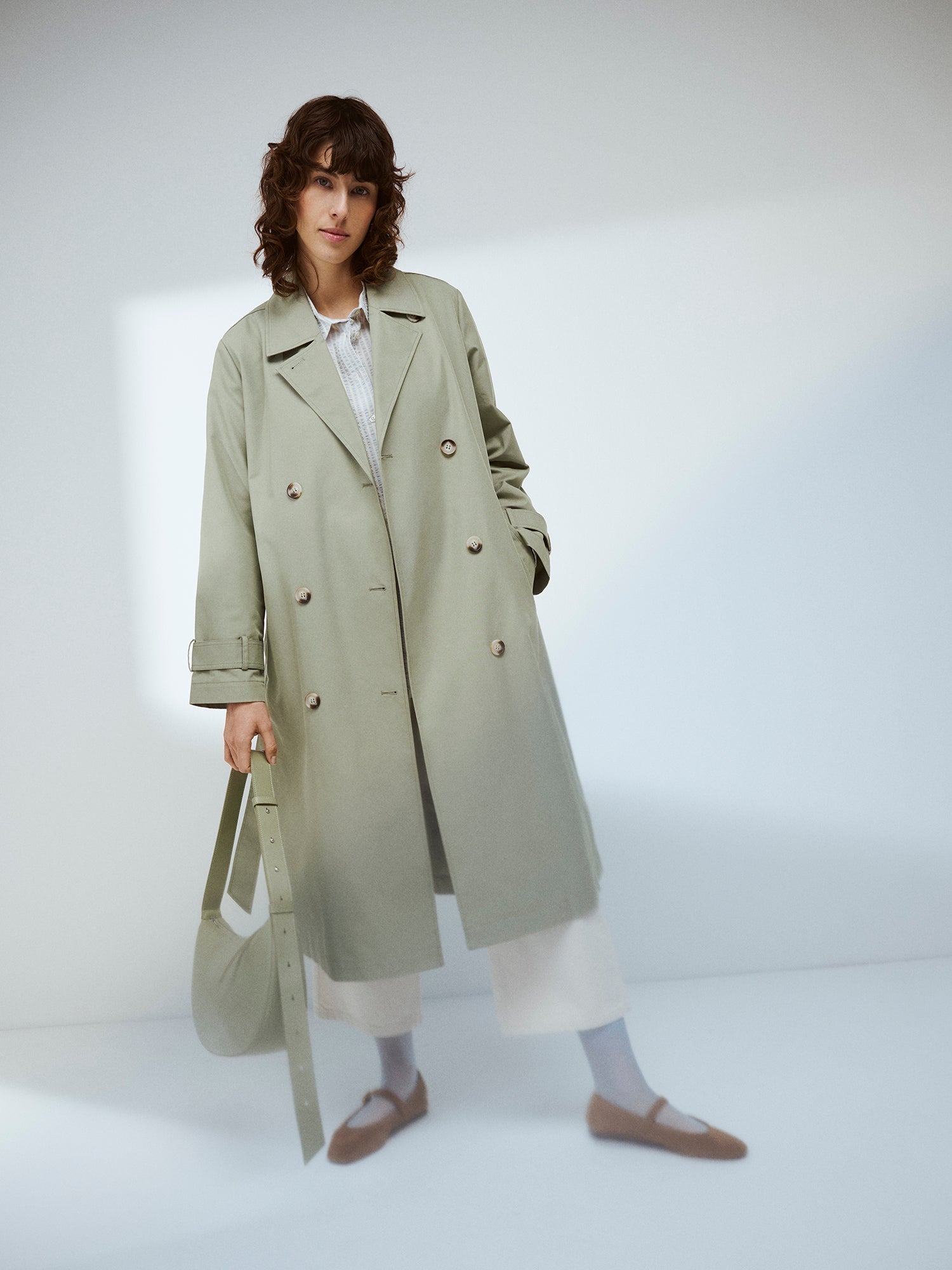 Nanson naisten klassisen tyylikäs vaaleanvihreä Trenssi-takki tummahiuksisen mallin päällä Olka Kuu -laukun kanssa.