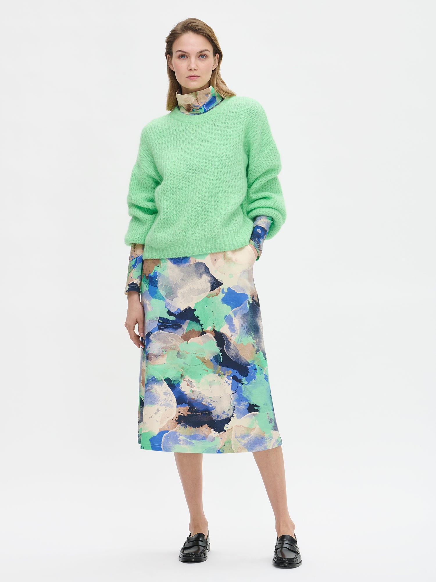 Karamelli naisten vaaleanvihreä neulepusero, jossa pyöreä pääntie ja täyspitkät hihat, sekoitta, jossa on mohairia, villaa, polyamidia ja hieman elastaania. Kuvattuna mallin päällä kuosillisen mekon kanssa.