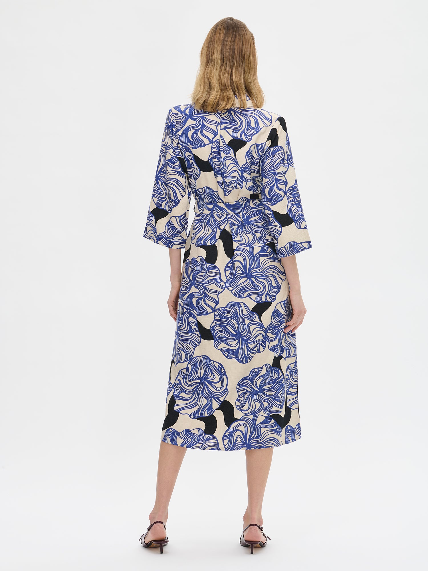 Naisten Kosmo-mekossa yhdistyy pelkistetty klassinen malli ja näyttävä sinisävyinen kuosi. Mekon istuvuus on helppo säätää sopivaksi vyöllä ja siinä on myös käytännölliset taskut. Kuvassa mallin päällä korkokenkien kanssa takaa kuvattuna.