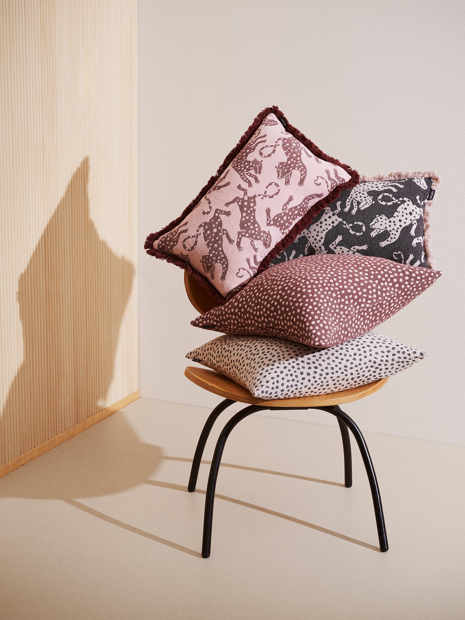 Muru-tyynynpäällinen beigessä ja punaruskeassa värissä kuvattuna muiden samansävyisten koristetyynyjen kanssa tuolin päällä.