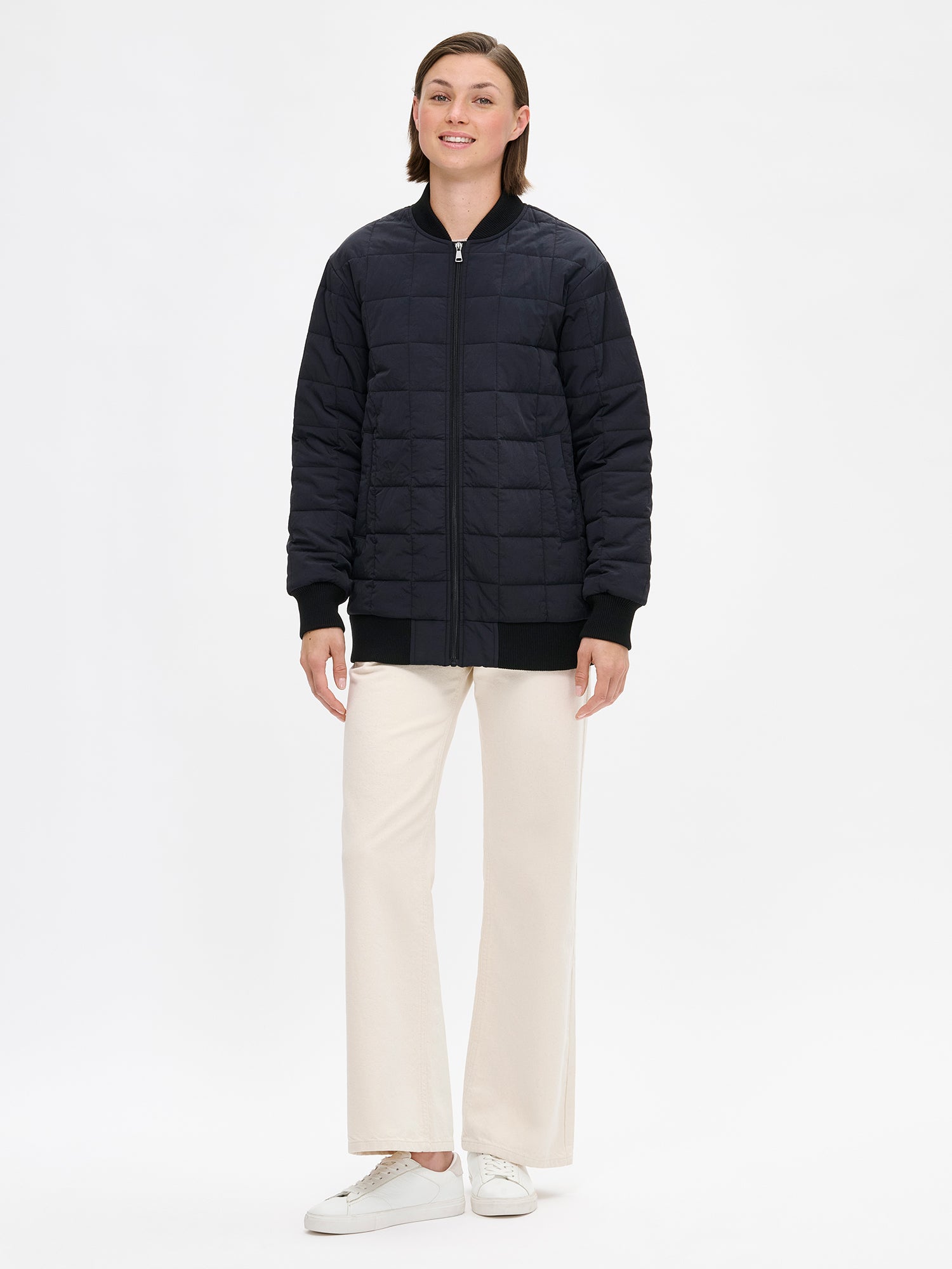 Nanson naisten rento Merje bomber tikkitakki kevyellä vanulla. Takin pääntiellä, hihansuissa ja helmassa on neulosresori. Edessä on vetoketju ja taskut. Takin olkalinja on pudotettu. Mallin päällä kiinni kuvattuna valkoisten farkkujen kanssa.