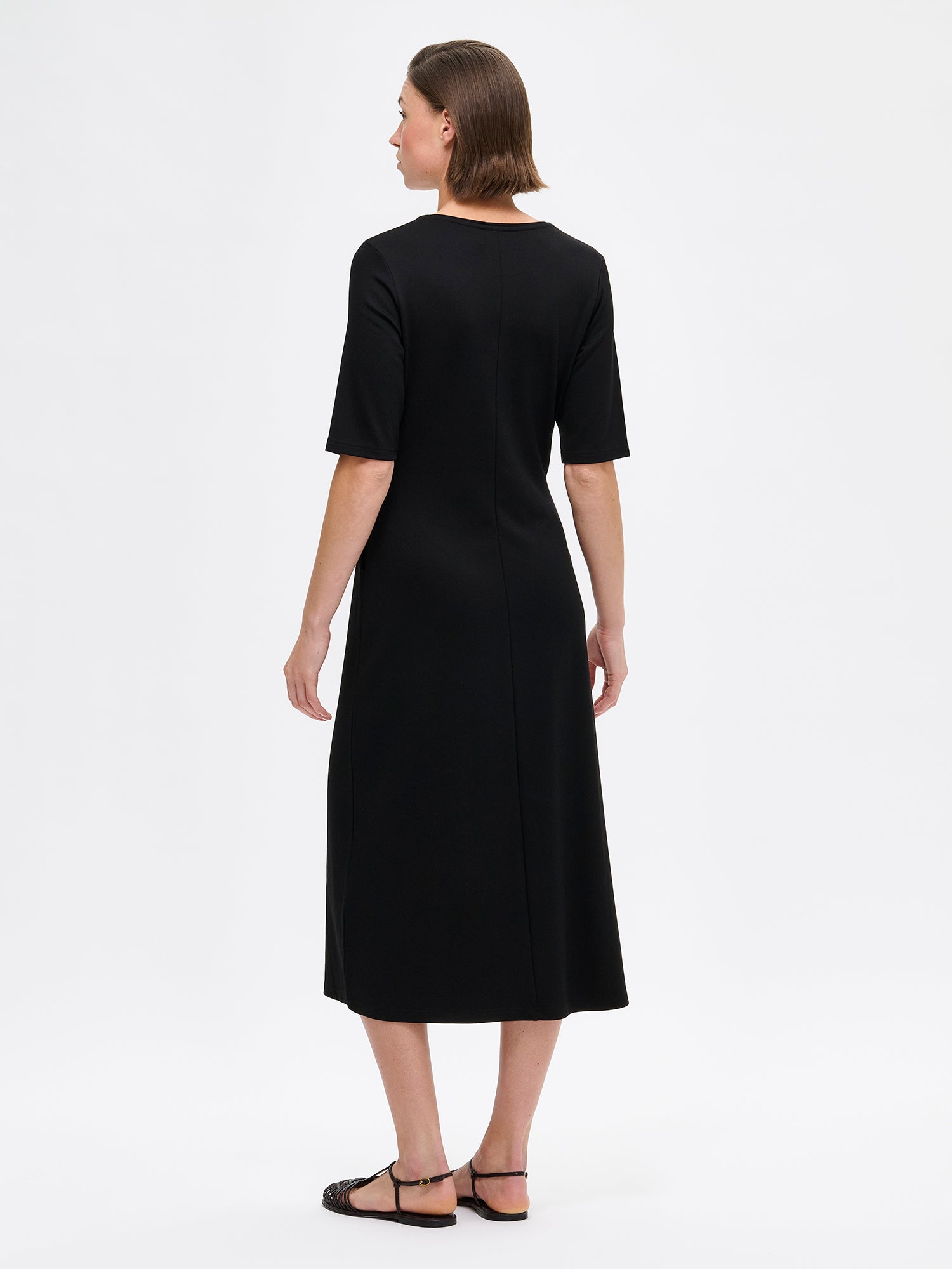 Naisten yksinkertaisen tyylikäs ja ajaton Roma-mekko mallin päällä sandaalien kanssa takaa kuvattuna.