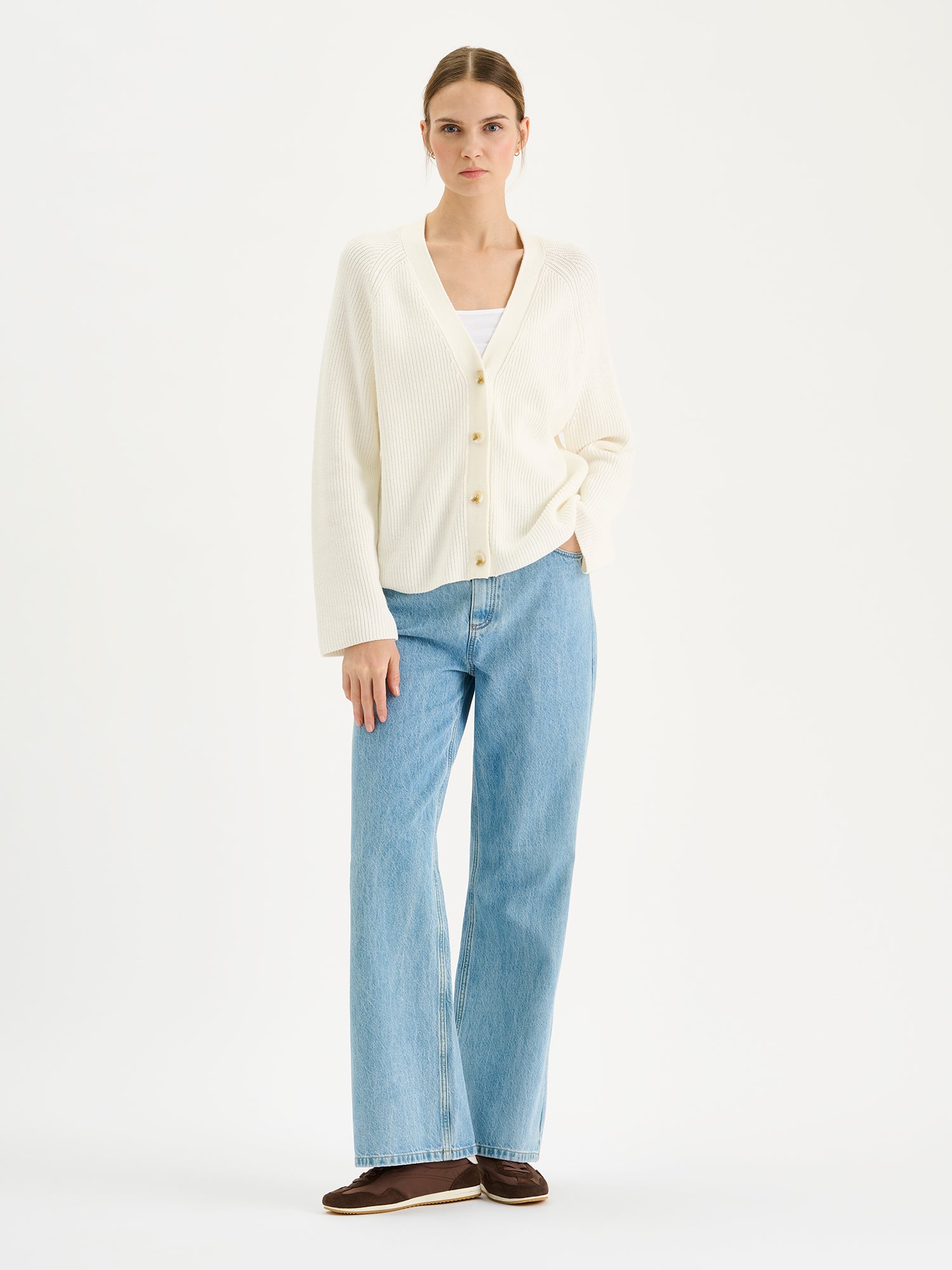 Naisten tyylikäs ja monikäyttöinen Kaveri-neuletakki pehmeän luonnonvalkoisessa sävyssä mallin päällä farkkujen kanssa.