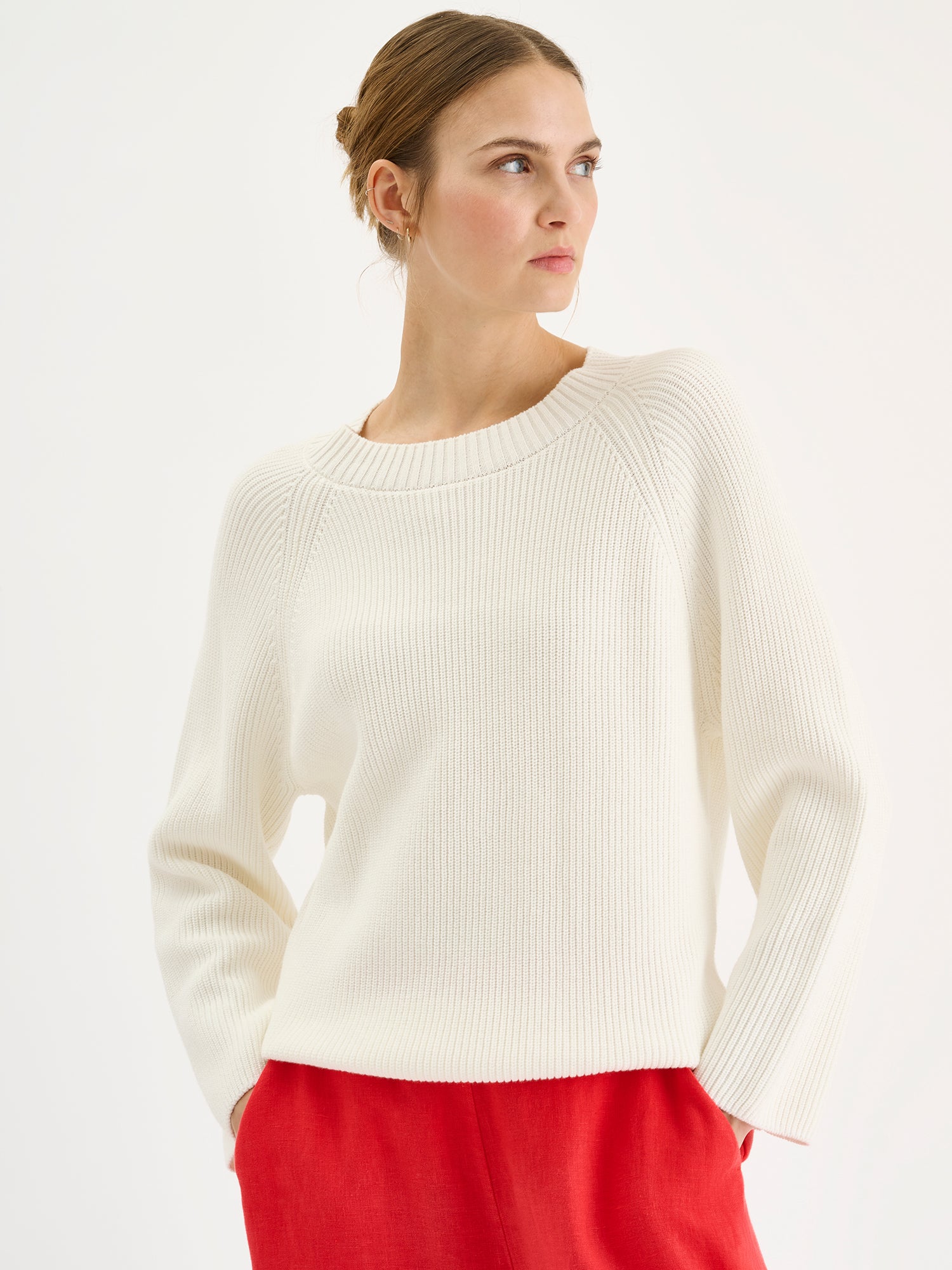 Naisten tyylikäs pehmeän luonnonvalkoinen Kaveri-neulepaita mallin päällä punaisten pellavahousujen kanssa lähikuvassa.