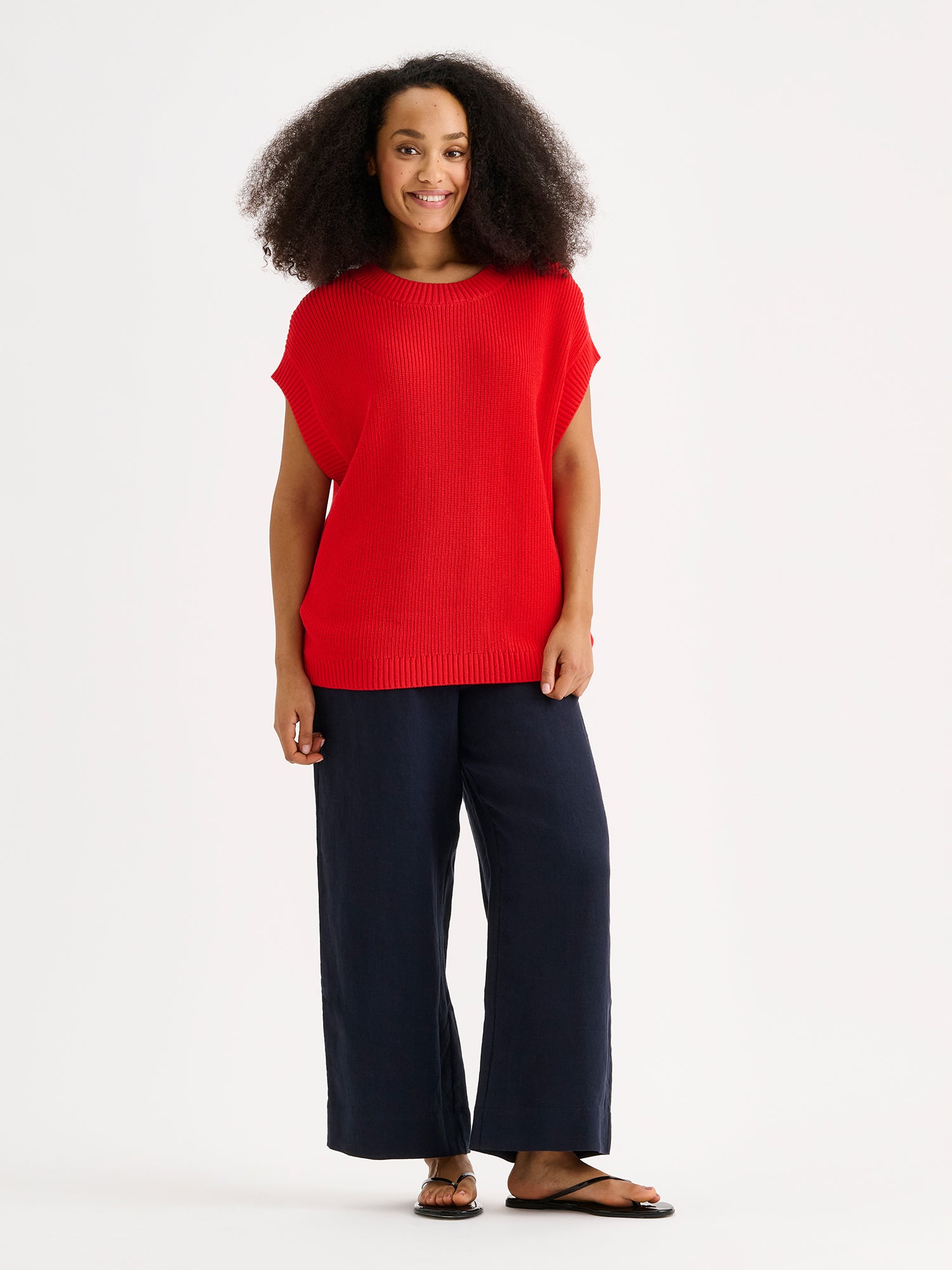 Nanson naisten tyylikäs punainen puuvillainen Kaveri-neuleliivi mallin päällä sinisten pellavahousujen kanssa.