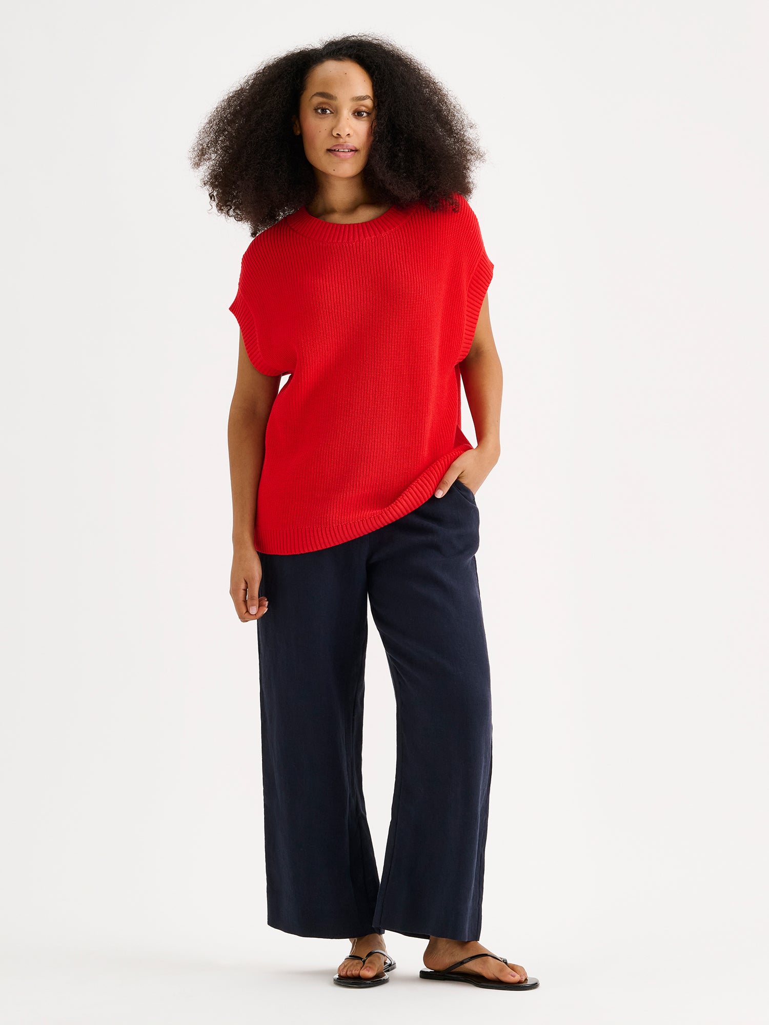 Nanson naisten tyylikäs punainen puuvillainen Kaveri-neuleliivi mallin päällä sinisten pellavahousujen kanssa.