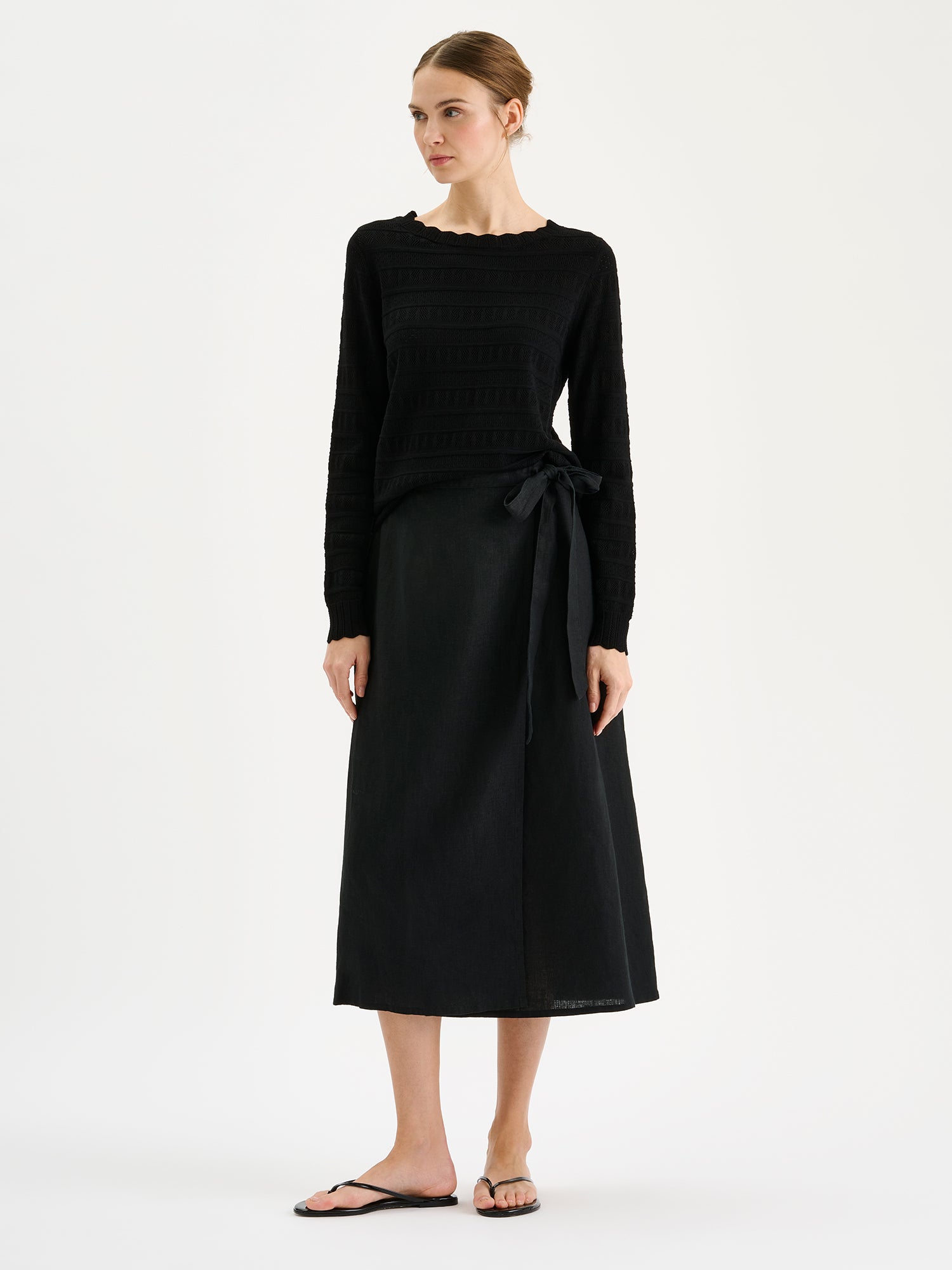 Nanson naisten pitkähihainen musta Koru-neulepaita pitsineuloksesta mallin päällä mustan hameen kanssa