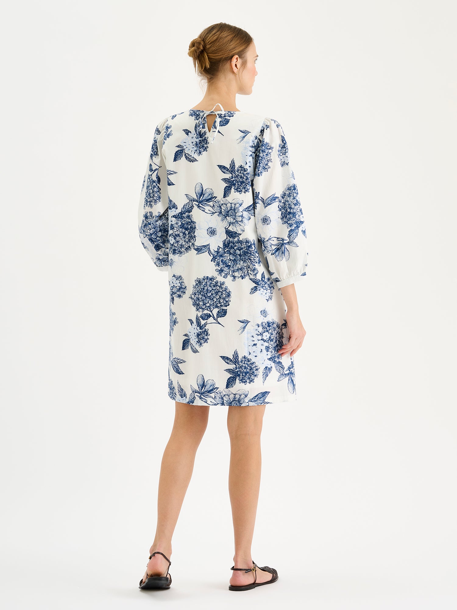 Naisten hurmaava sinivalkoinen kuosillinen Palatsi-mekko mallin päällä sandaalien kanssa takaa kuvattuna.