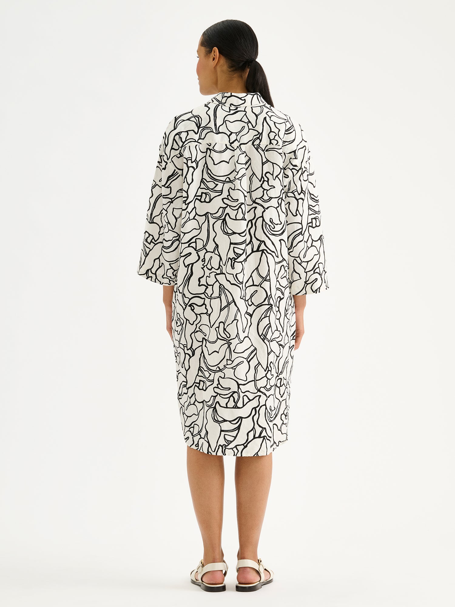 Naisten mukavan rento Iiris-paitamekko, jossa on tyylikäs ja näyttävä mustavalkoinen kukkakuosi mallin päällä sandaalien kanssa takaa kuvattuna.