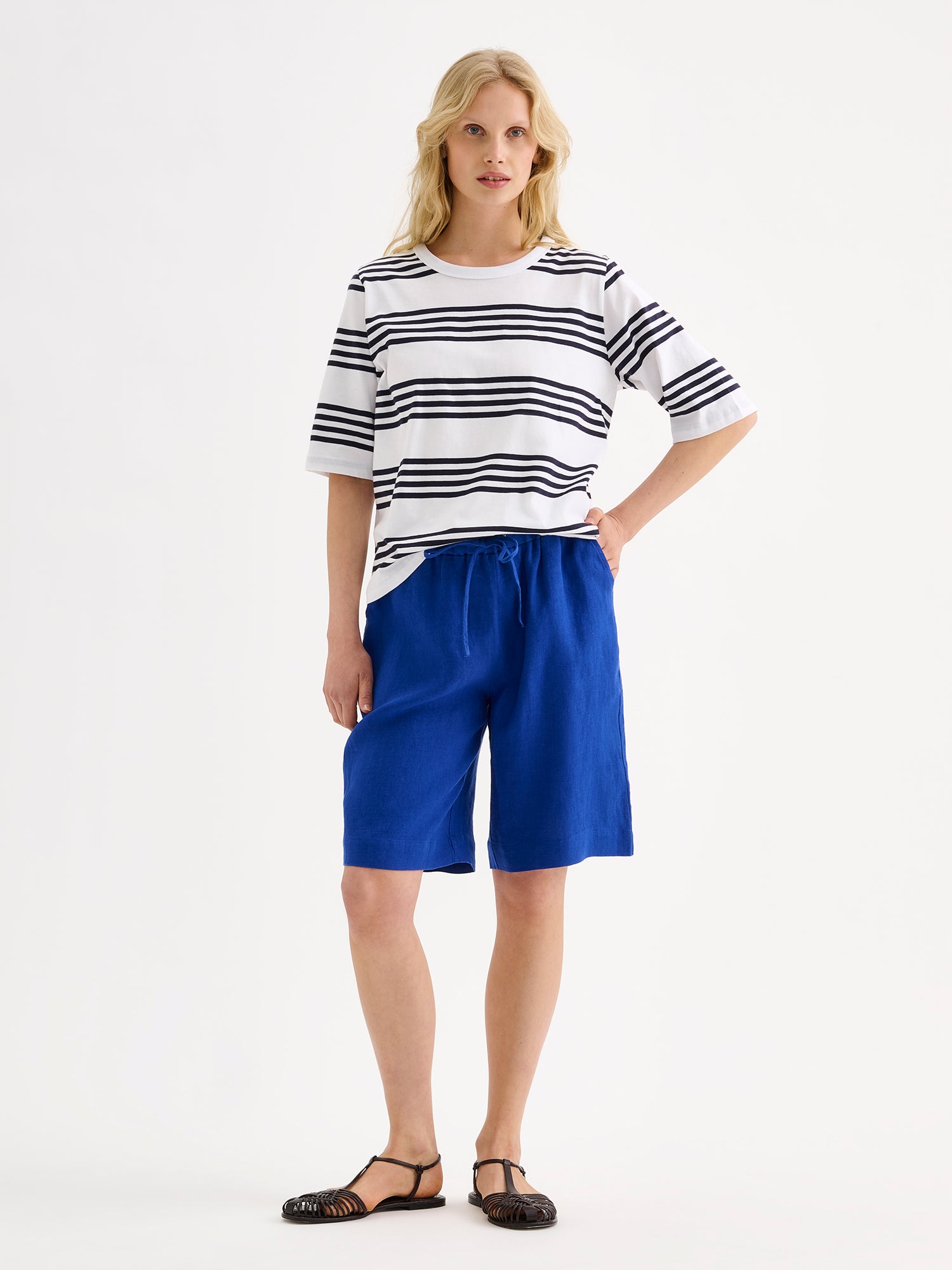 Nanson naisten raikkaan raidallinen sinivalkoinen Merina- t-paita mallin päällä sinisten pellavashortsien kanssa.