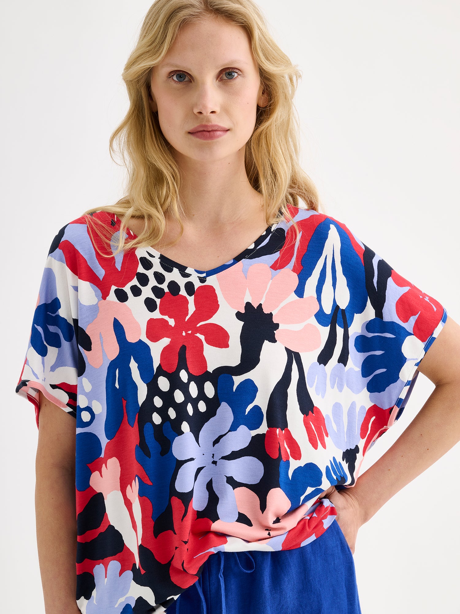 Nanson naisten laadukas ja mukava Koralli-trikoopusero, jossa on raikkaan värikäs kuosi mallin päällä sinisten pellavahousujen kanssa lähikuvassa.