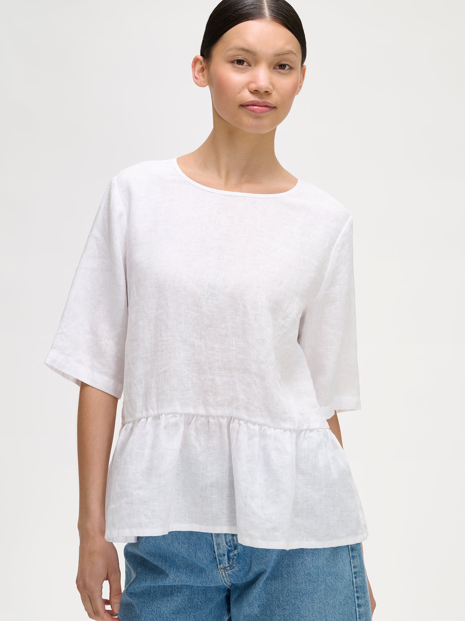 Nanson naisten kaunis ja ihanan rennon mallinen valkoinen Liisu-pellavapusero, jonka helmassa on viehättävä frilla, mallin päällä farkkushortsien kanssa, lähikuvassa.