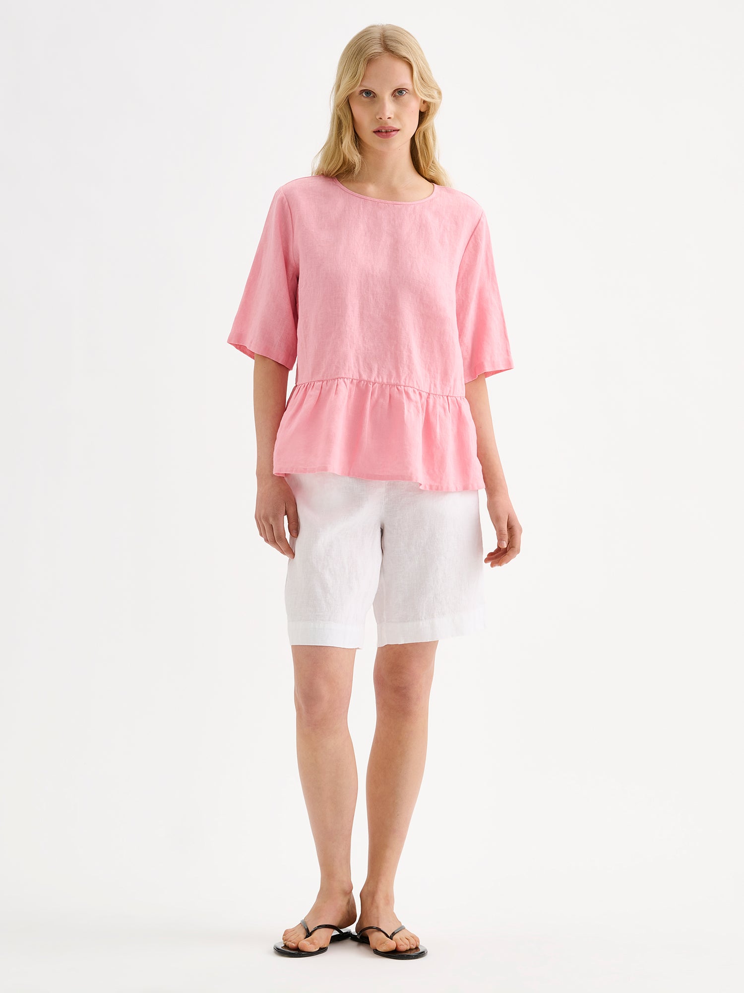 Nanson naisten kaunis ja ihanan rennon mallinen vaaleanpunainen Liisu-pellavapusero, jonka helmassa on viehättävä frilla, mallin päällä valkoisten pellavashortsien kanssa.