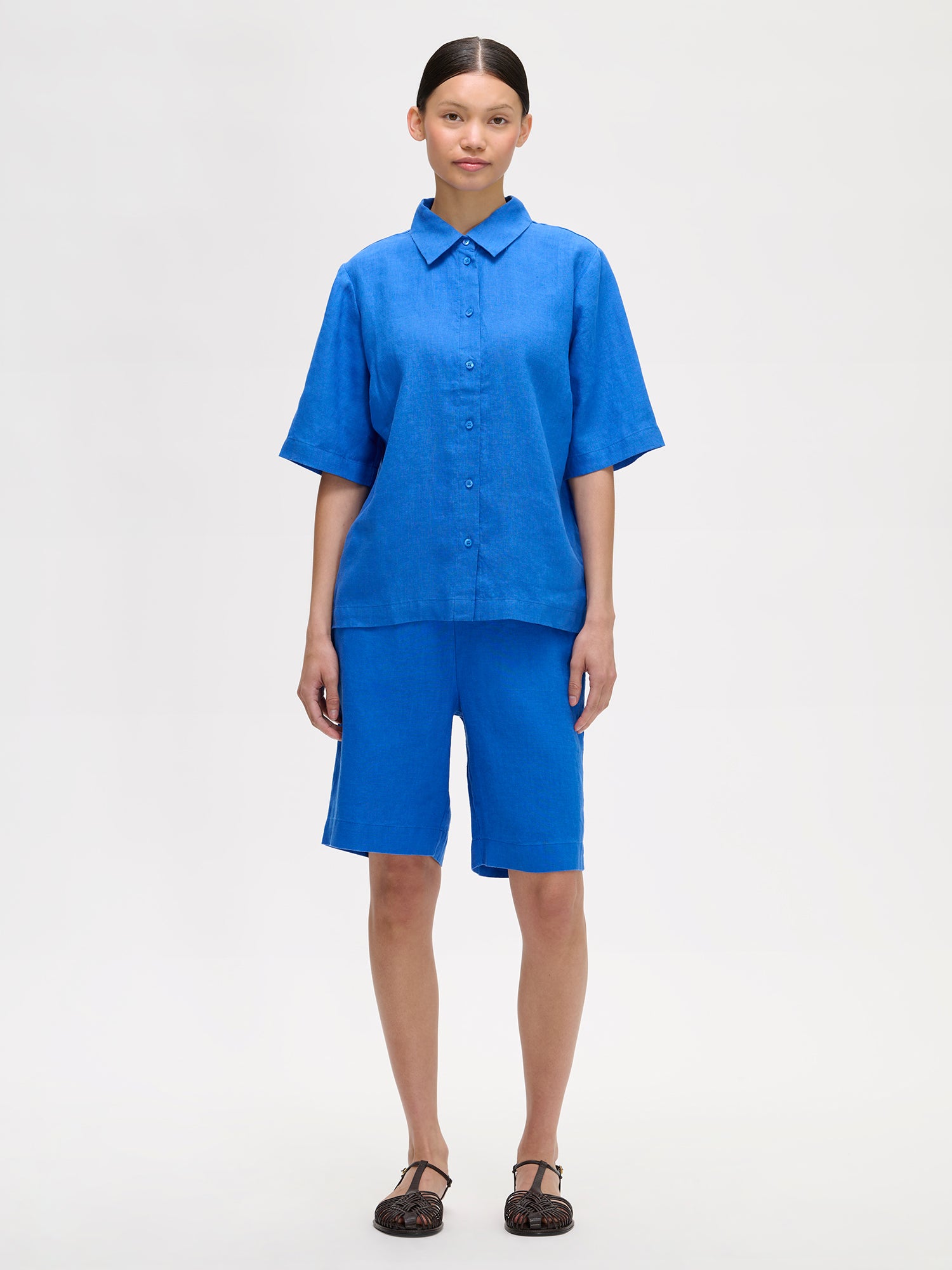 Naisten rento sininen Liine-paitapusero, joka on valmistettu hengittävästä pellavasta, mallin päällä pellavashortsien kanssa.