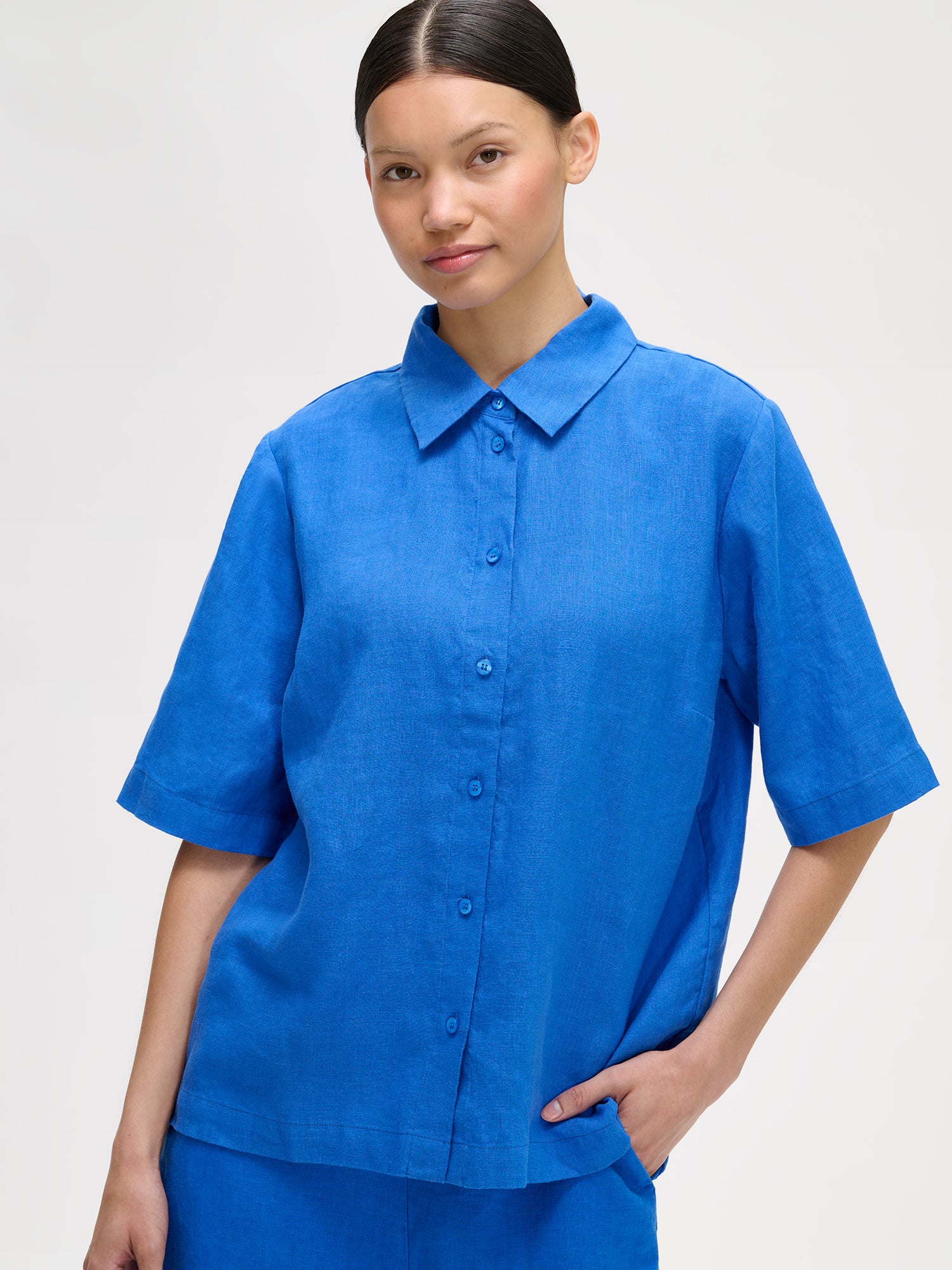 Naisten rento sininen Liine-paitapusero, joka on valmistettu hengittävästä pellavasta, mallin päällä pellavashortsien kanssa, lähikuvassa.