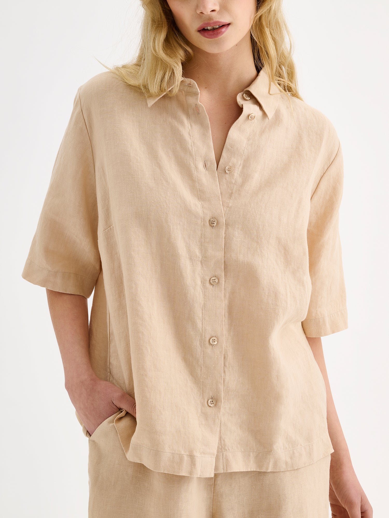 Naisten rento beige Liine-paitapusero, joka on valmistettu hengittävästä pellavasta, mallin päällä pellavashortsien kanssa, lähikuvassa.