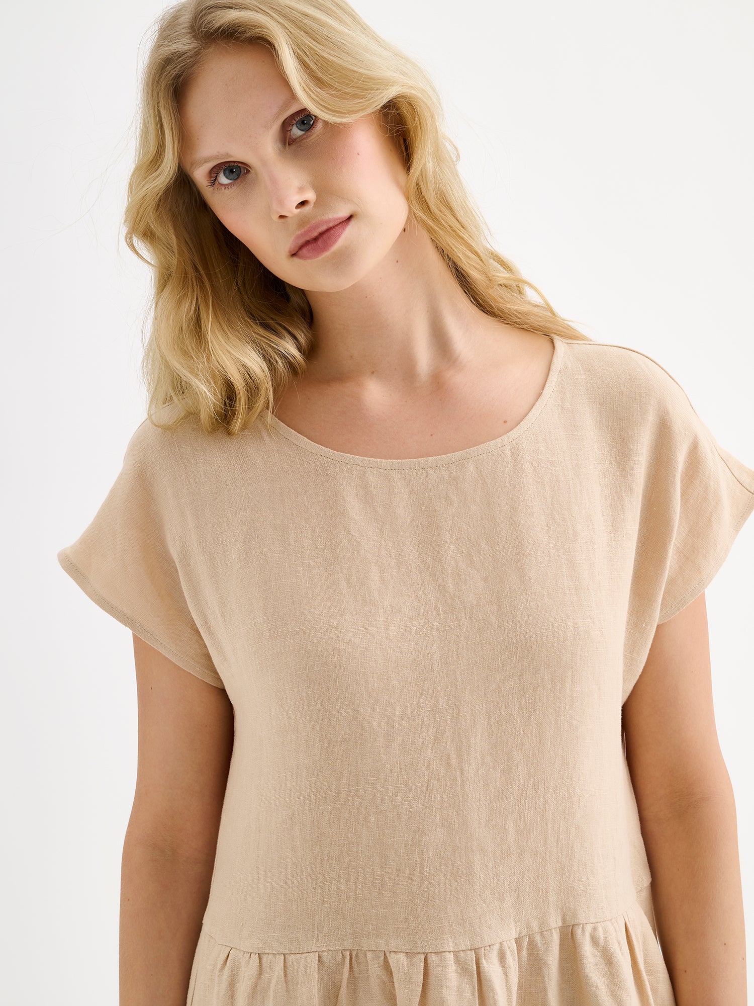 Nanson naisten rento midipituinen lyhythihainen beige Saari-pellavamekko taskuilla, rypytetyllä helmalla ja ovaalin mallisella pääntiellä mallin päällä lähikuvassa.