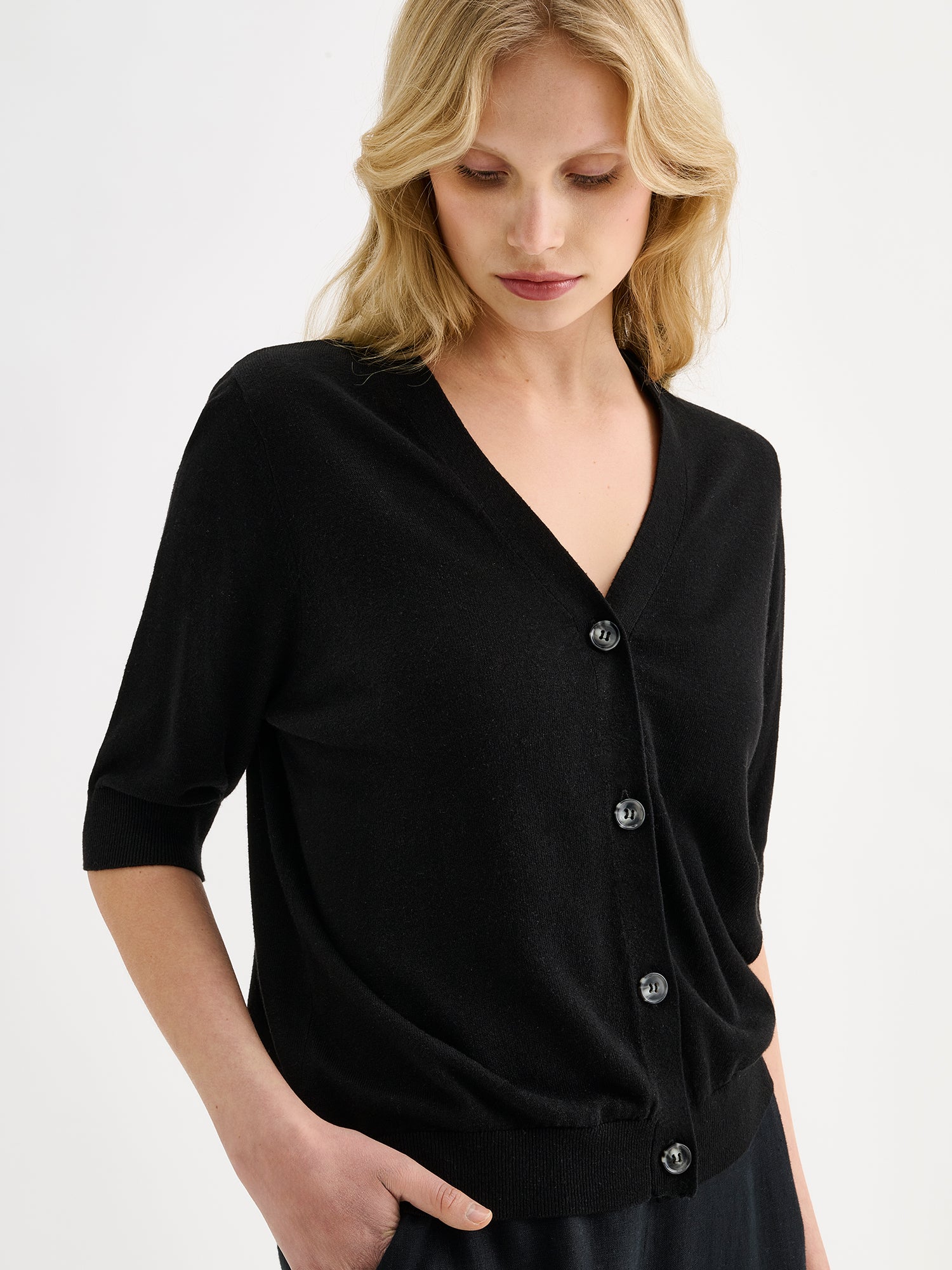 Nanson naisten musta puolihihainen Karina-neuletakki mallin päällä mustien pellavahousujen kanssa, lähikuvassa