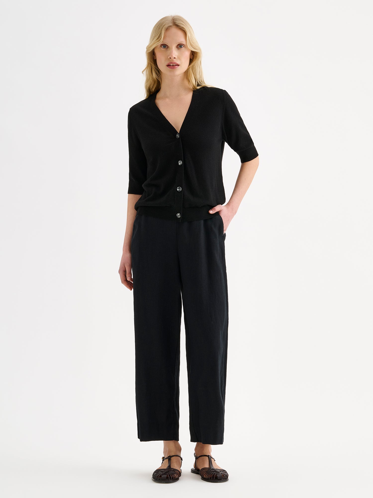 Nanson naisten musta puolihihainen Karina-neuletakki mallin päällä mustien pellavahousujen kanssa.