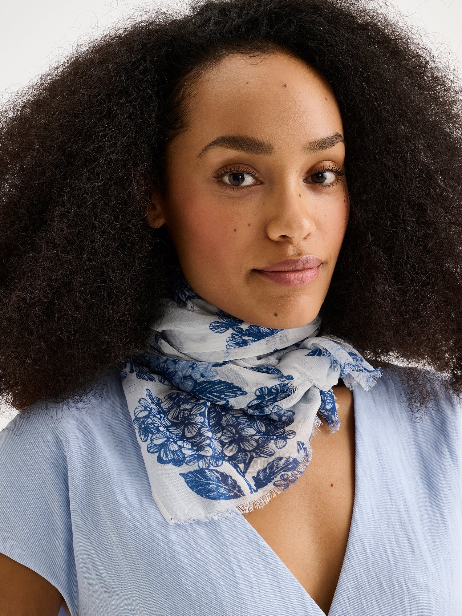 Naisten tyylikäs kuviollinen Palatsi-huivi, jossa on herkkä sininen kukkakuosi valkoisella pohjasävyllä mallin päällä vaaleansinisen Nizza-liivin kanssa lähikuvassa.