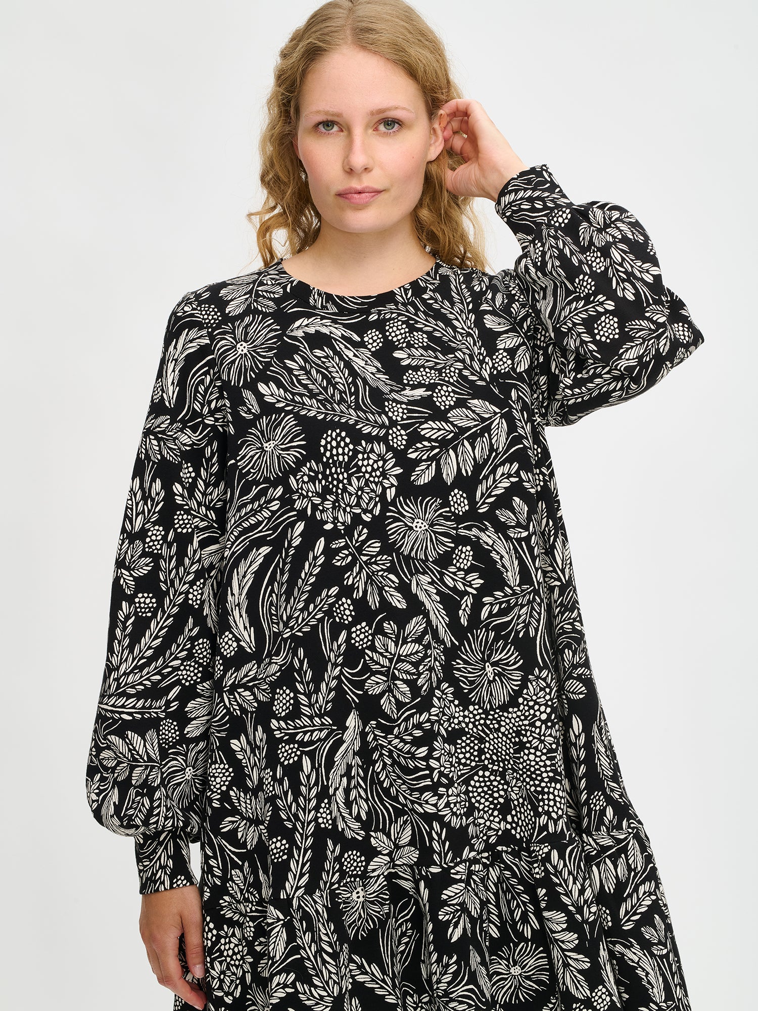 Nanson naisten mustavalkoinen Floora-mekko, poimutettu helma ja kasviaiheinen kuosi, pitkät hihat, mallin yllä puolivartalokuvassa.