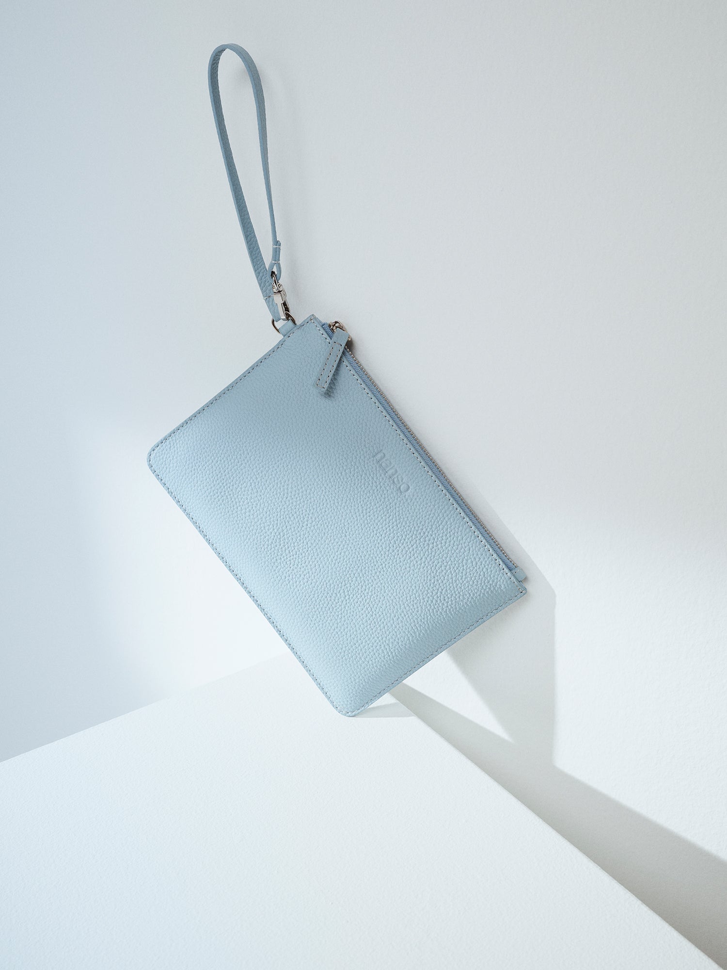 Nanson käytännöllinen ja tyylikäs vaaleansininen Naru Pieni- laukku toimii niin lompakkona kuin pikkulaukkuna. Nahkalaukussa on lyhyt kantohihna, jonka saa kiinnitettyä myös isomman laukun hihnaan. Laukun päällä on metallinen vetoketju. Nanson logo on painettu nahan pintaan laukun etu puolelle. Tuotekuva edestä.