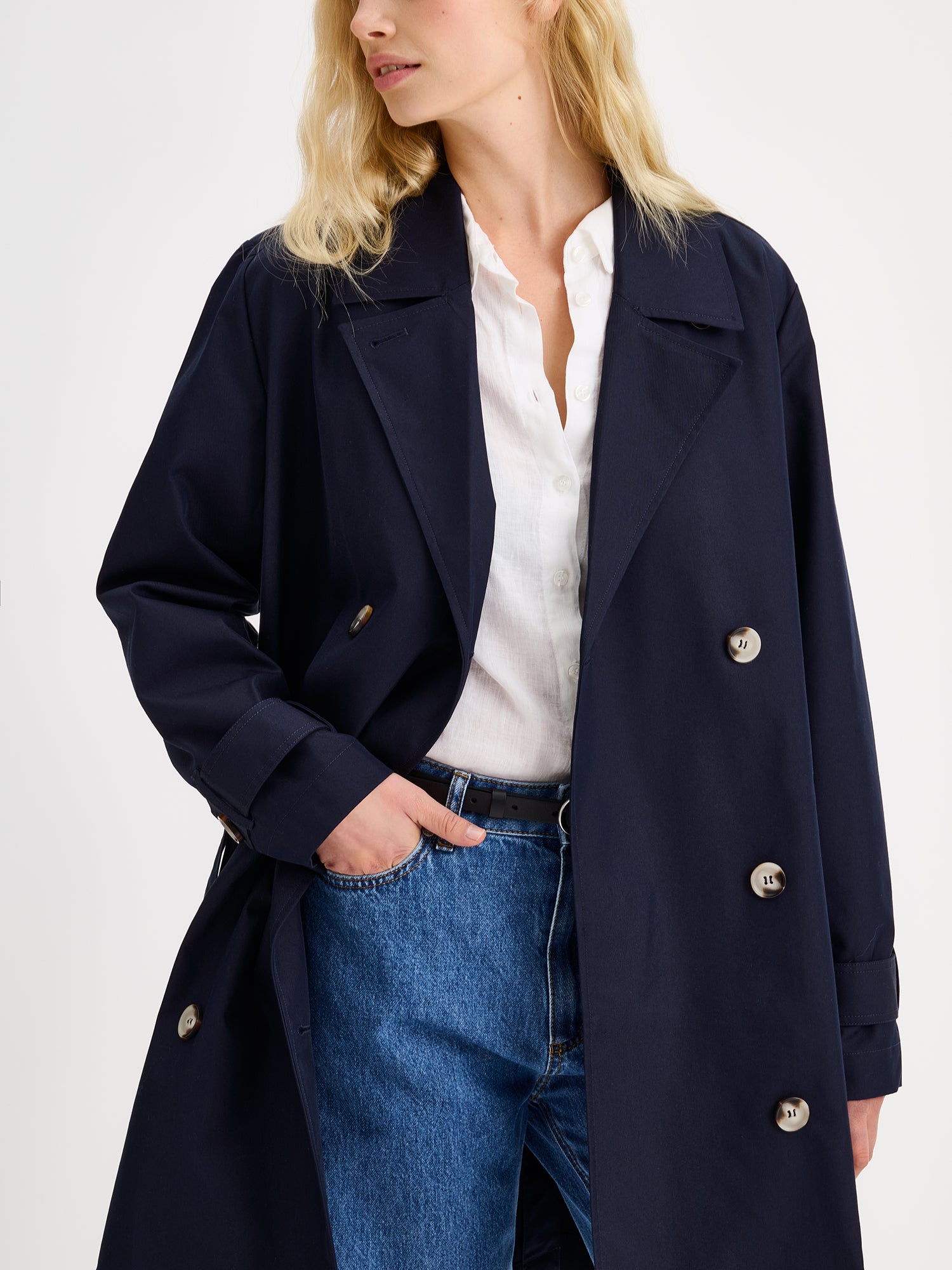 Nanson naisten tummansininen Midi Trenssi-takki vaaleahiuksisen mallin päällä lähikuvassa takki avattuna.