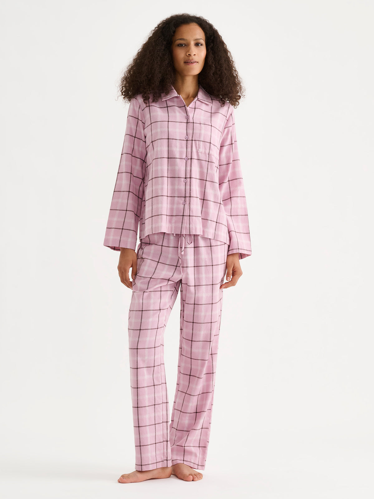 Nanson naisten pehmoinen flanellinen Tuulikki-pyjamapaita, jossa klassinen vaaleanpunainen ruudullinen flanellikangas, kaulukset, rintatasku ja nappilista, mallin päällä saman sarjan housujen kanssa.