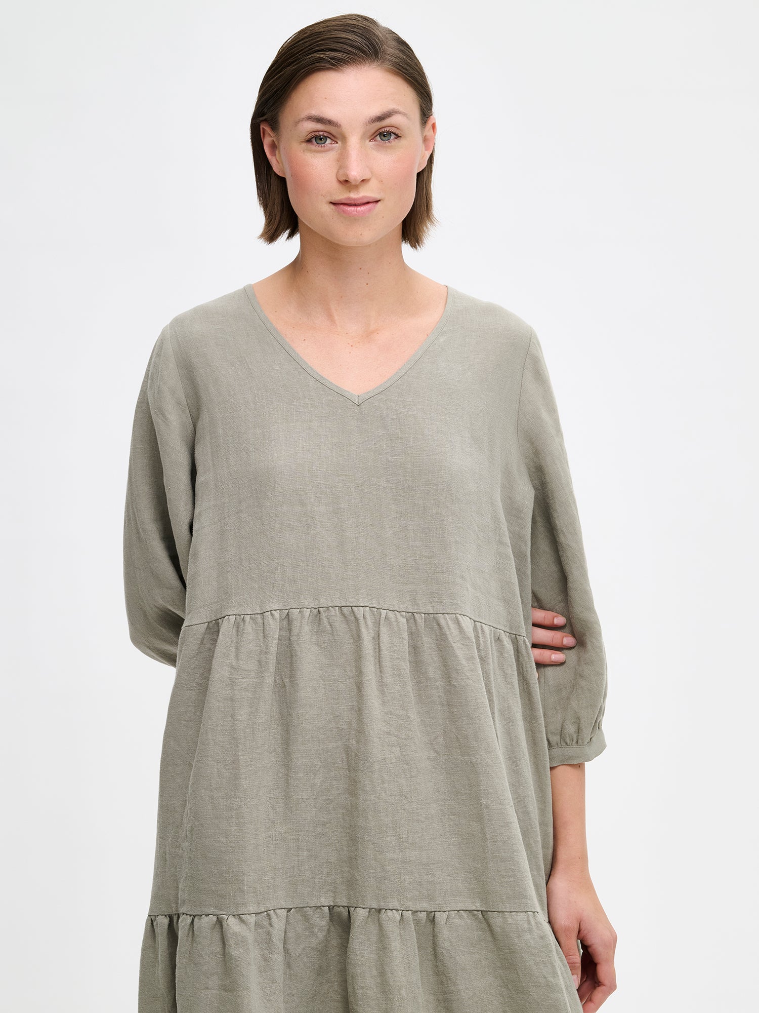 Nanson vihreä midipituinen frillahelmainen Saralivia pellavamekko, jossa on kauniit 3/4 hihat, sivutaskut ja V-pääntie. Pellavamekon istuvuus on väljä ja materiaali on hengittävä. Kuvassa mallin päällä läheltä kuvattuna.