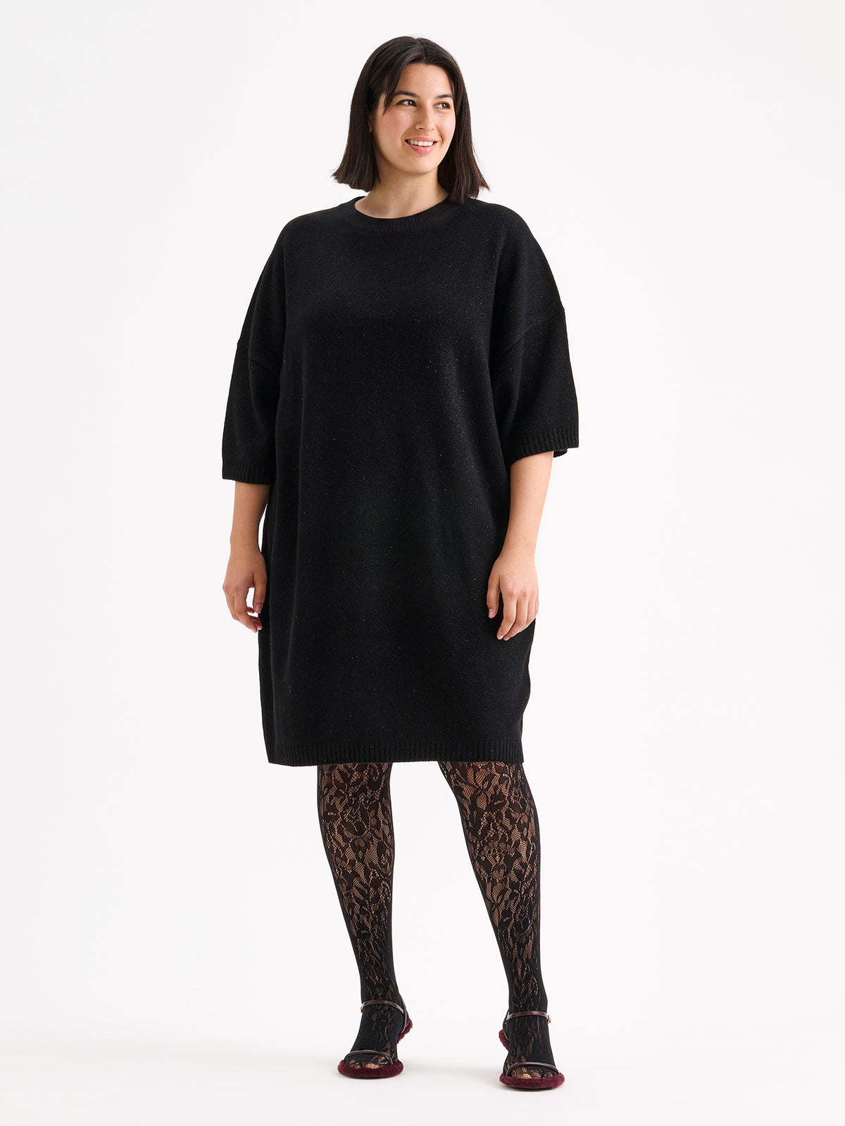 Nanson naisten rento, hieman oversized-mallinen musta kimaltava Lumine-neulemekko mallin päällä pitsisukkahousujen kanssa. | XL - 178cm