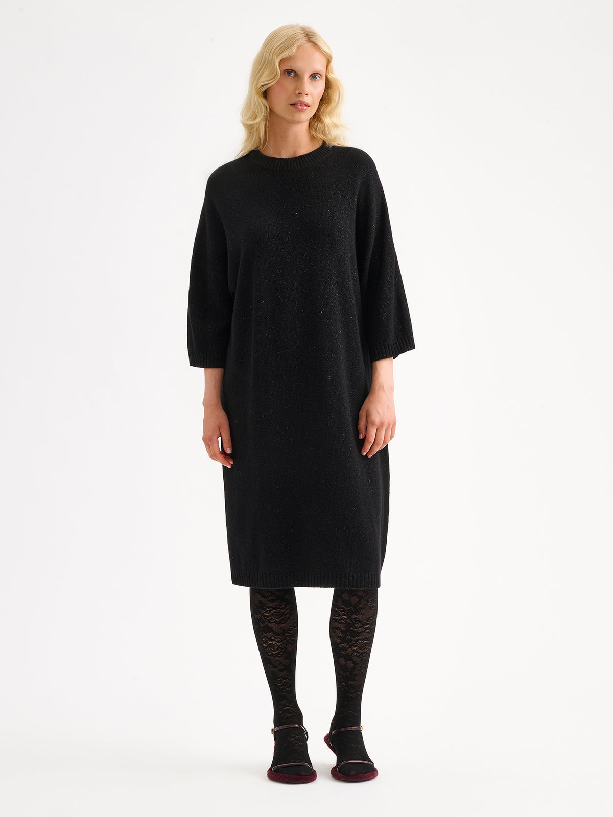 Nanson naisten rento, hieman oversized-mallinen musta kimaltava Lumine-neulemekko mallin päällä pitsisukkahousujen kanssa.