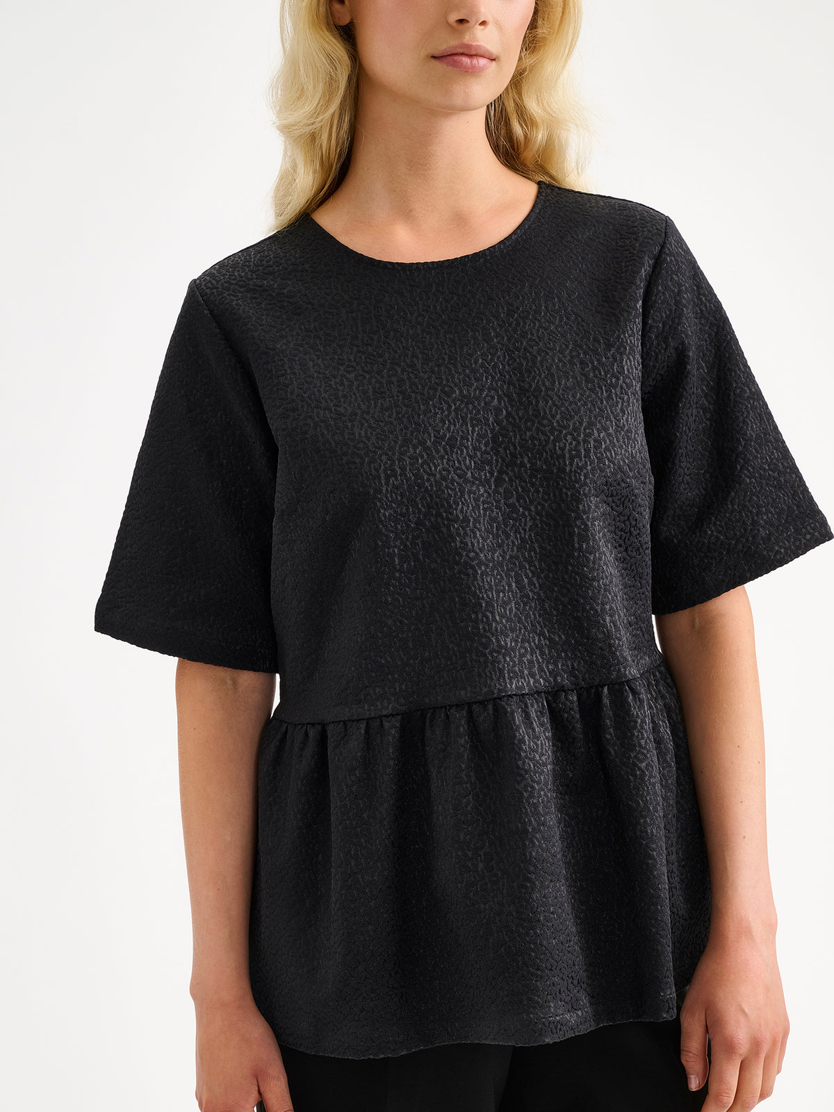 Nanson naisten kaunis ja juhlava musta Leora-pusero peplum-tyylisellä leikkauksella näyttävällä materiaalilla, mallin päällä mustien housujen kanssa.