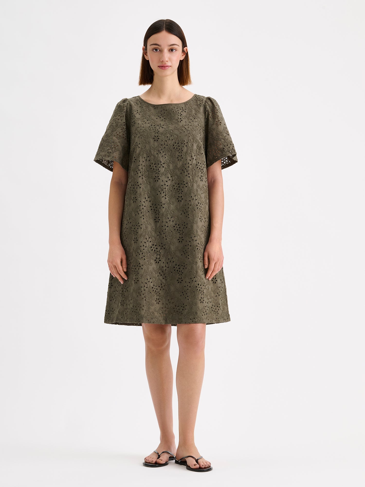 Nanson pitsikirjailtu oliivinvihreä Odette mekko mallin päällä sandaalien kanssa.
