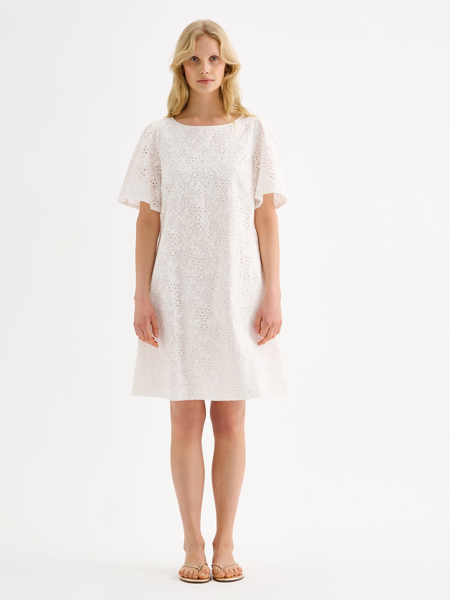 Nanson pitsikirjailtu luonnonvalkoinen Odette mekko mallin päällä sandaalien kanssa.