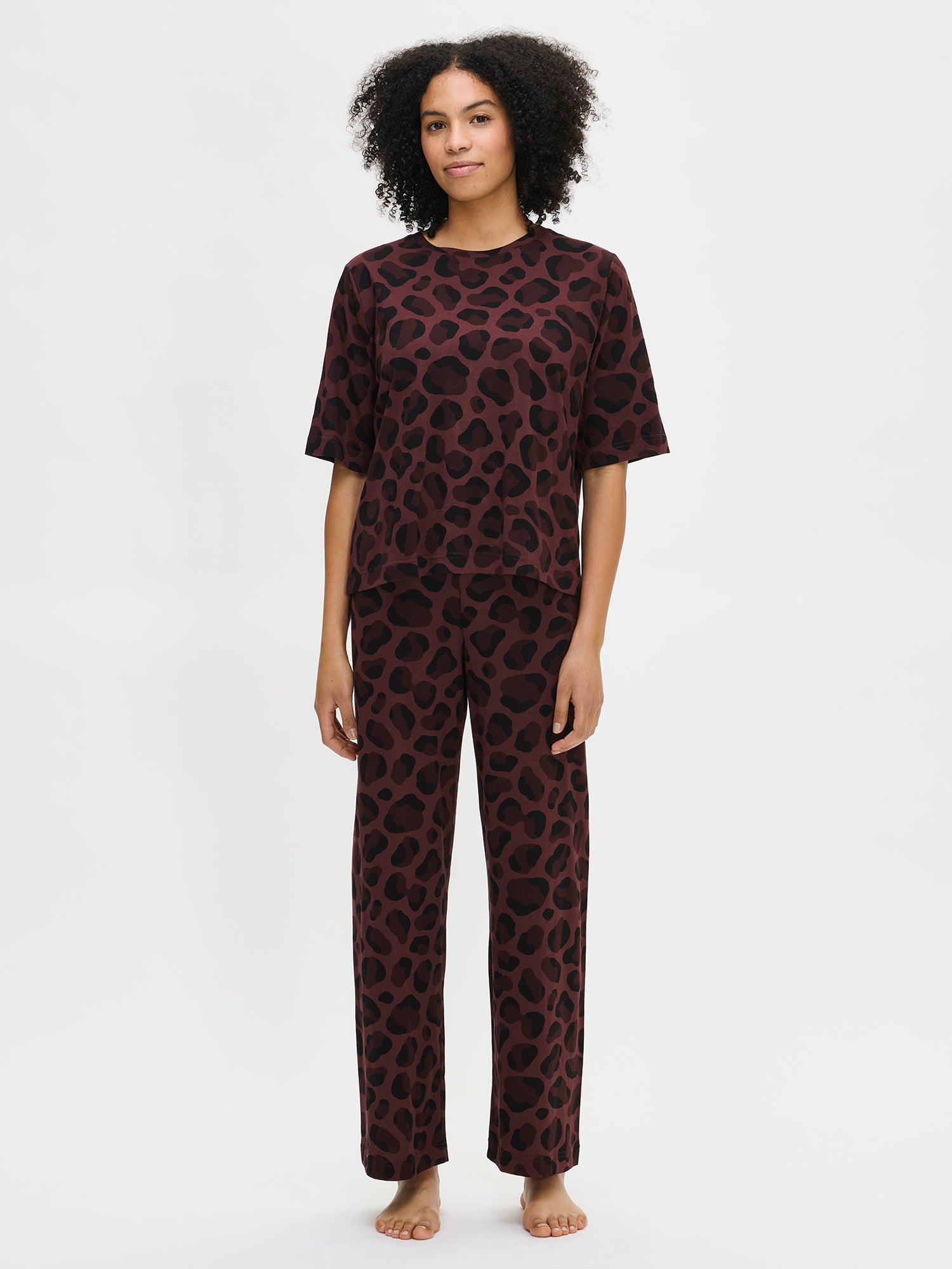Nanson naisten Pantteri-loungewear-asu, jossa ruskea Pantteri-T-paita ja yhteensopivat housut. Helma asettuu lantiolle. Mallin päällä kokovartalokuvassa edestä.