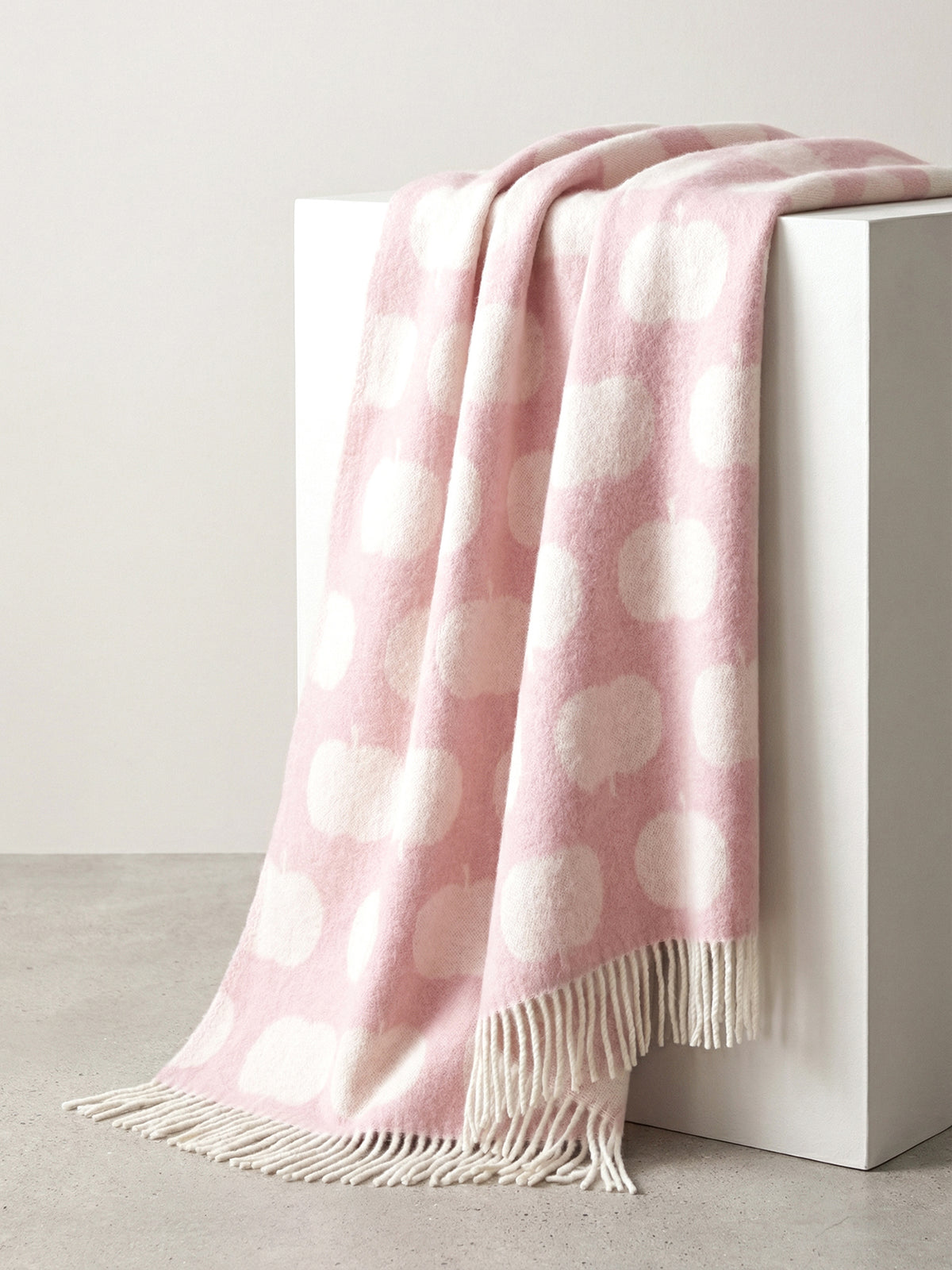 Nanson villainen roosan sävyinen Omppu-villahuopa, jonka lyhyitä sivuja koristaa kierrehapsut. Villahuopa on kudottu jacquard-tekniikalla. Kuvattuna laatikon päälle aseteltuna.