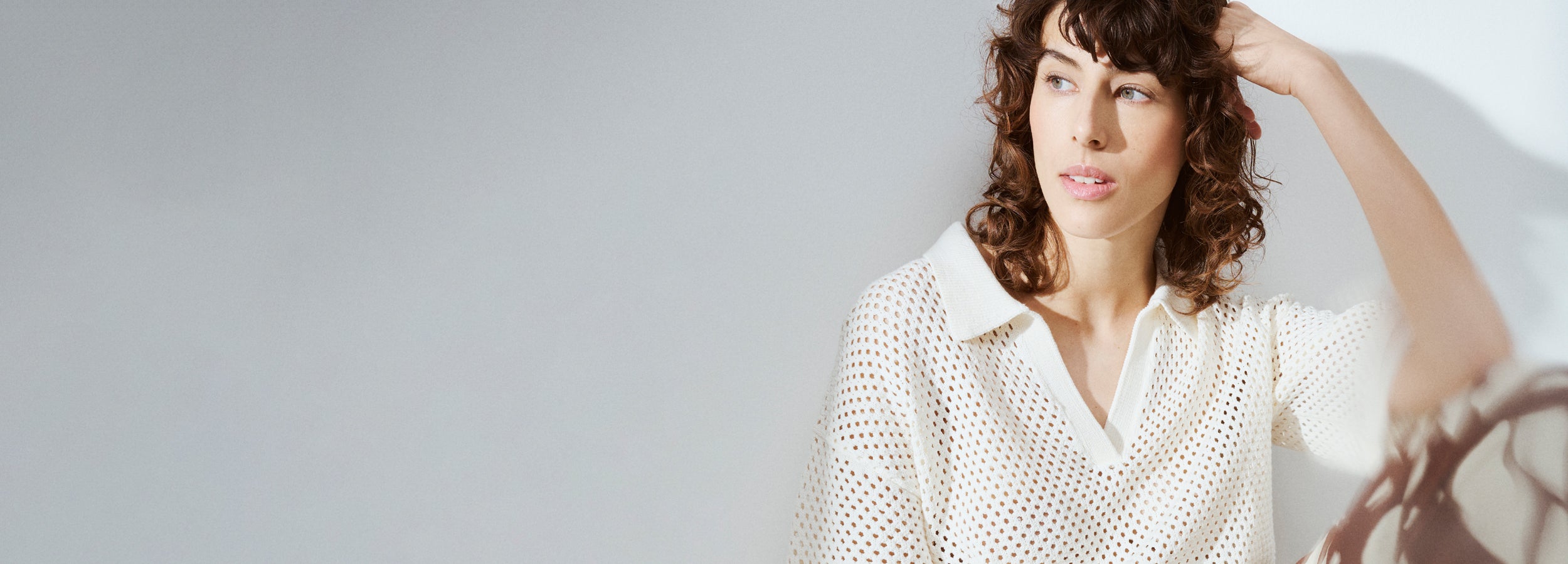 Nanson trendikäs reikäneuloksinen Aure pusero kiharahiuksisen mallin päällä brändikuvassa