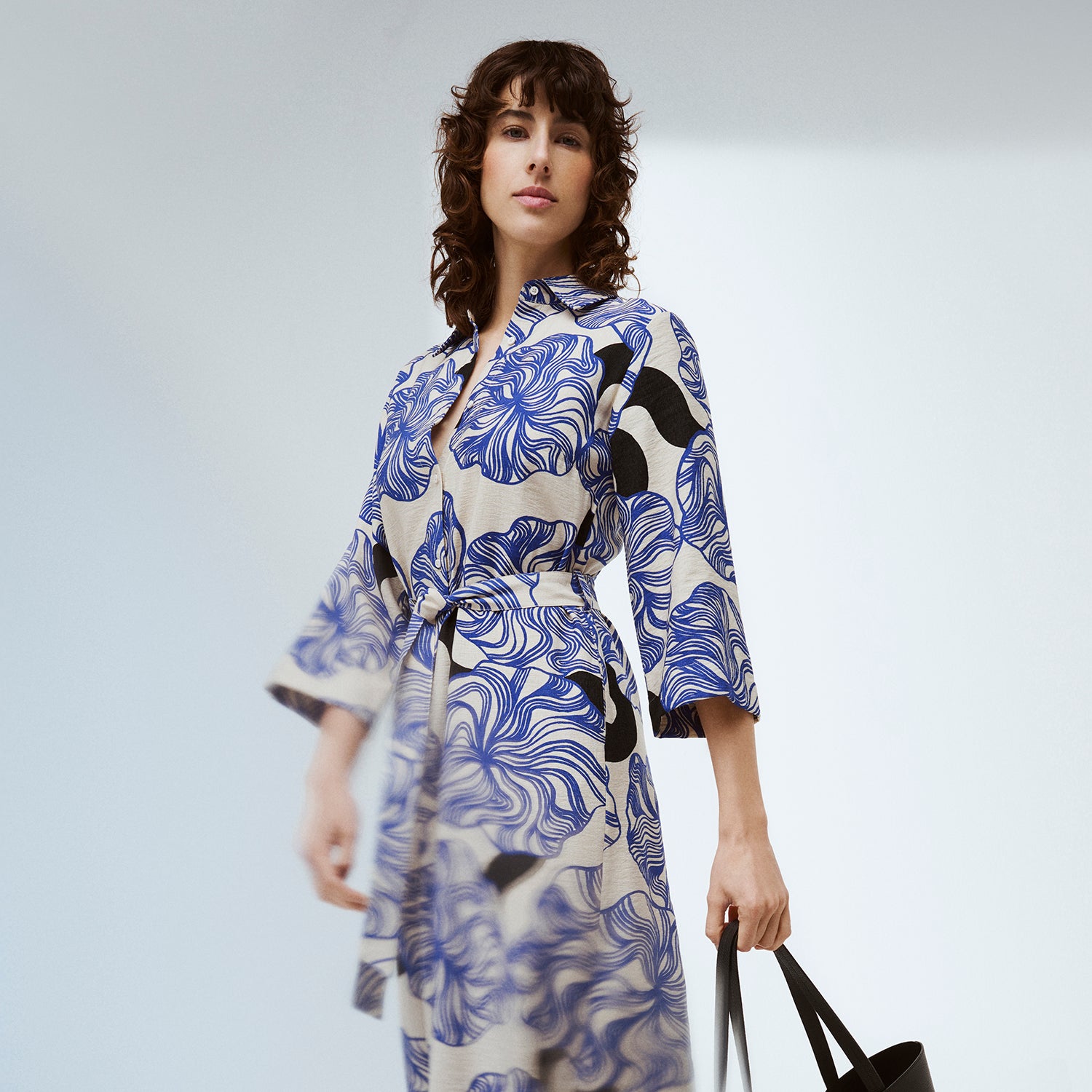 Naisen yllä Nanson kuosillinen Kosmo paitamekko, jossa sinisiä ja mustia kuvioita vaalealla pohjalla.